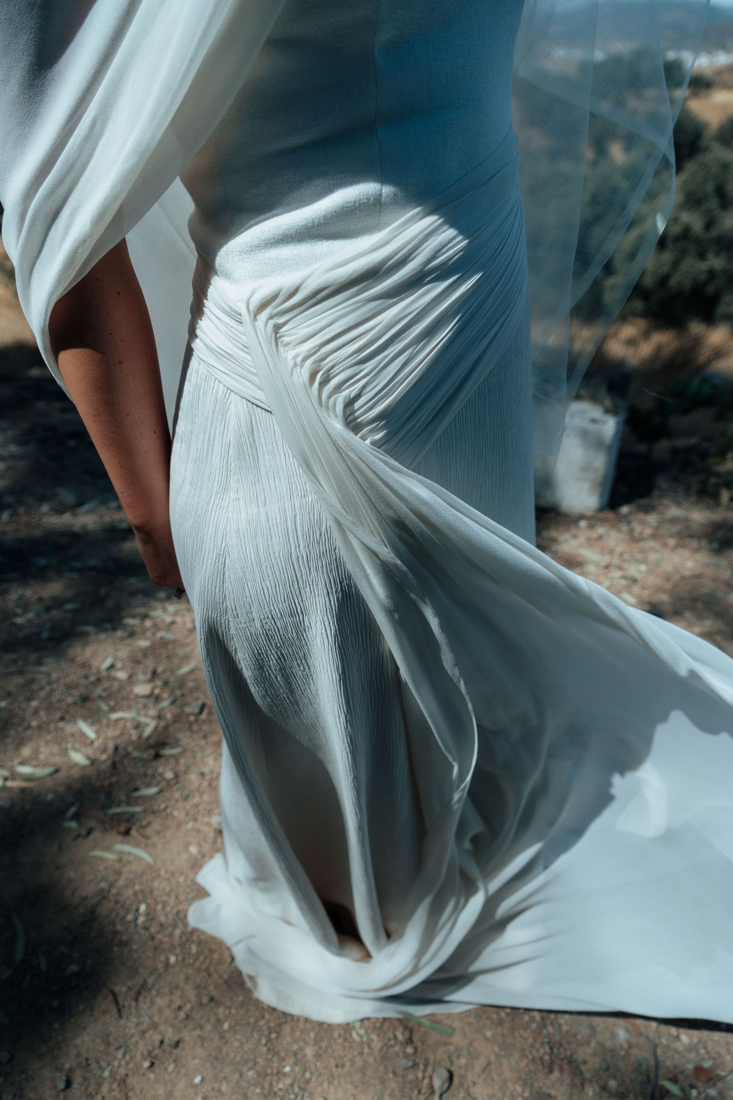 Close-up detail of elegant draped white wedding dress fabric flowing in natural outdoor light.