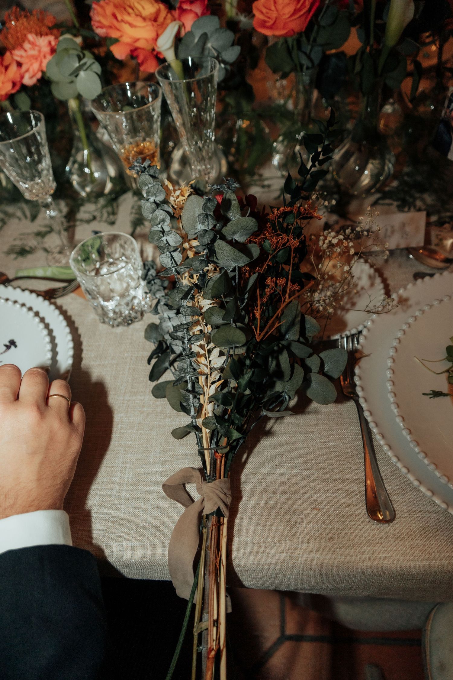 Groom placing eucalyptus botanical wedding favor bouquet on elegantly set reception table.