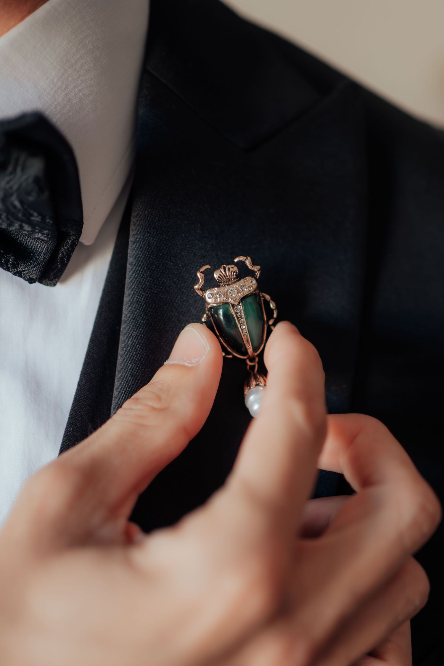 A close-up of a decorative green and gold beetle brooch boutonniere being pinned to a black lapel.