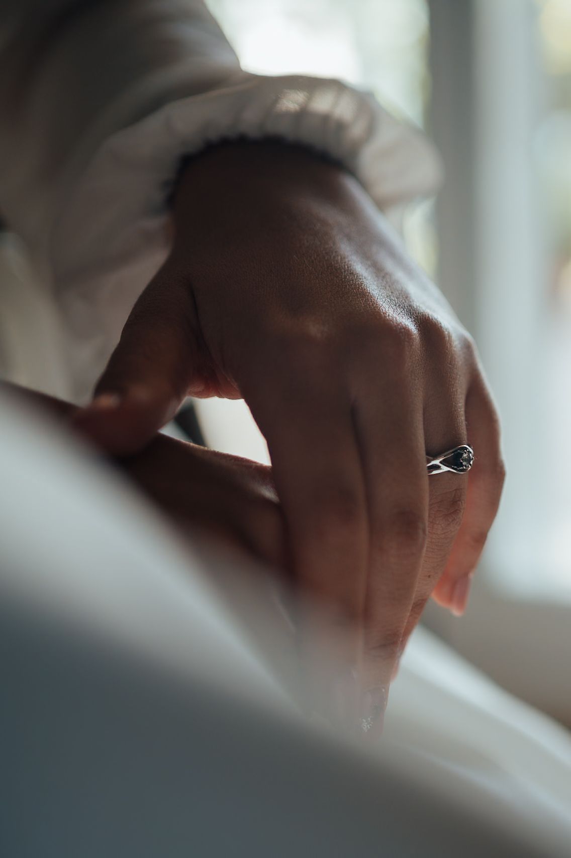 Close-up of a groom's hand wearing a silver ring, adjusting his white dress shirt cuff before the wedding ceremony.