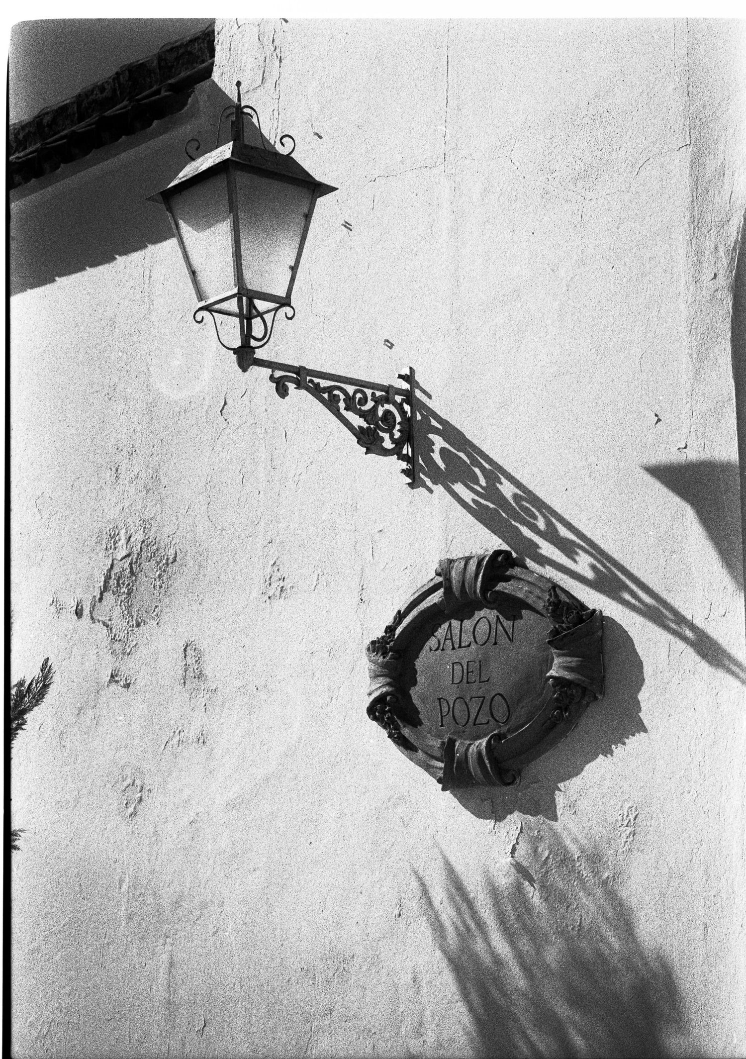 Black and white photo of Salon del Pozo sign with ornate wall lamp.