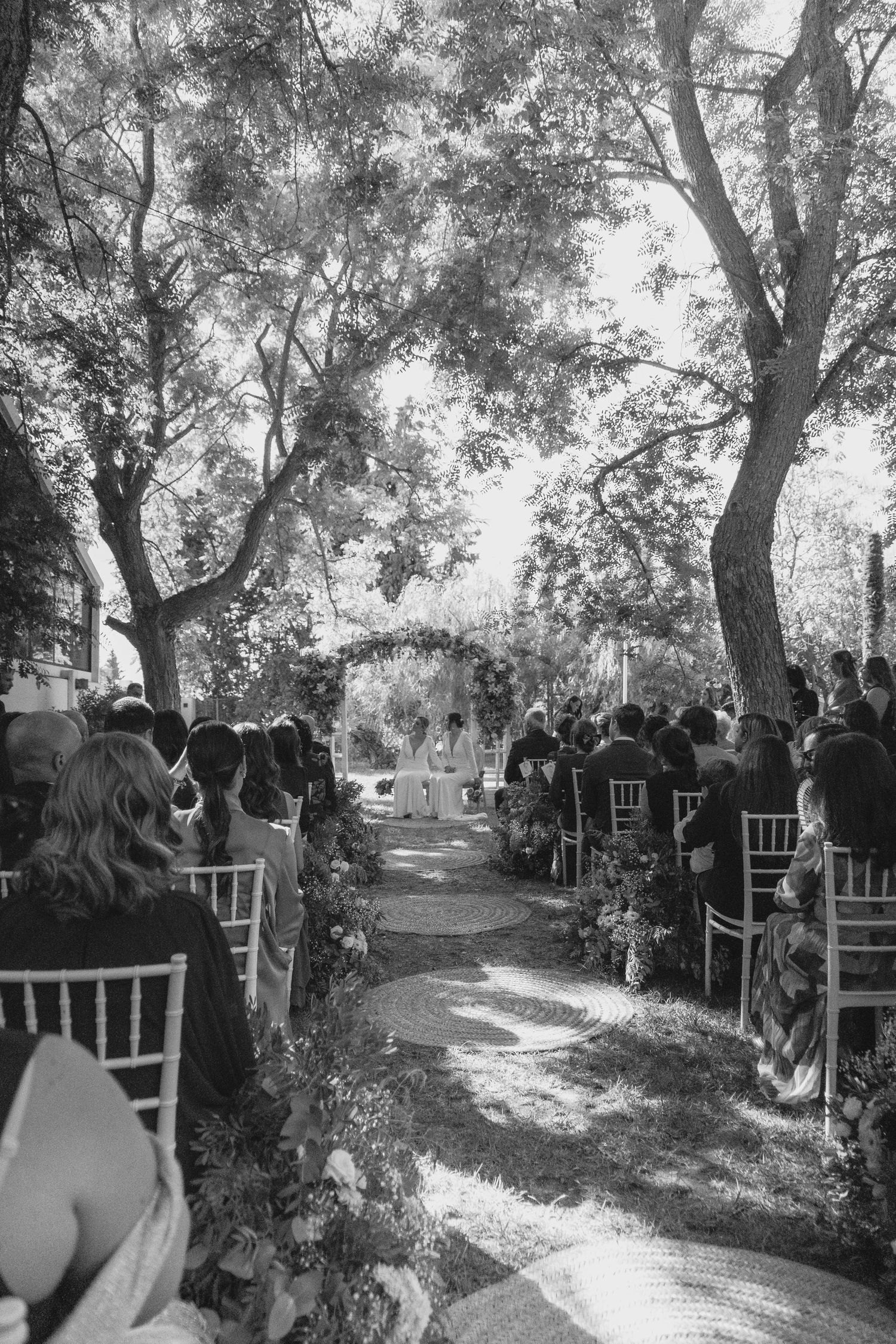 Black and white aerial view of outdoor wedding ceremony aisle lined with chairs under trees.
