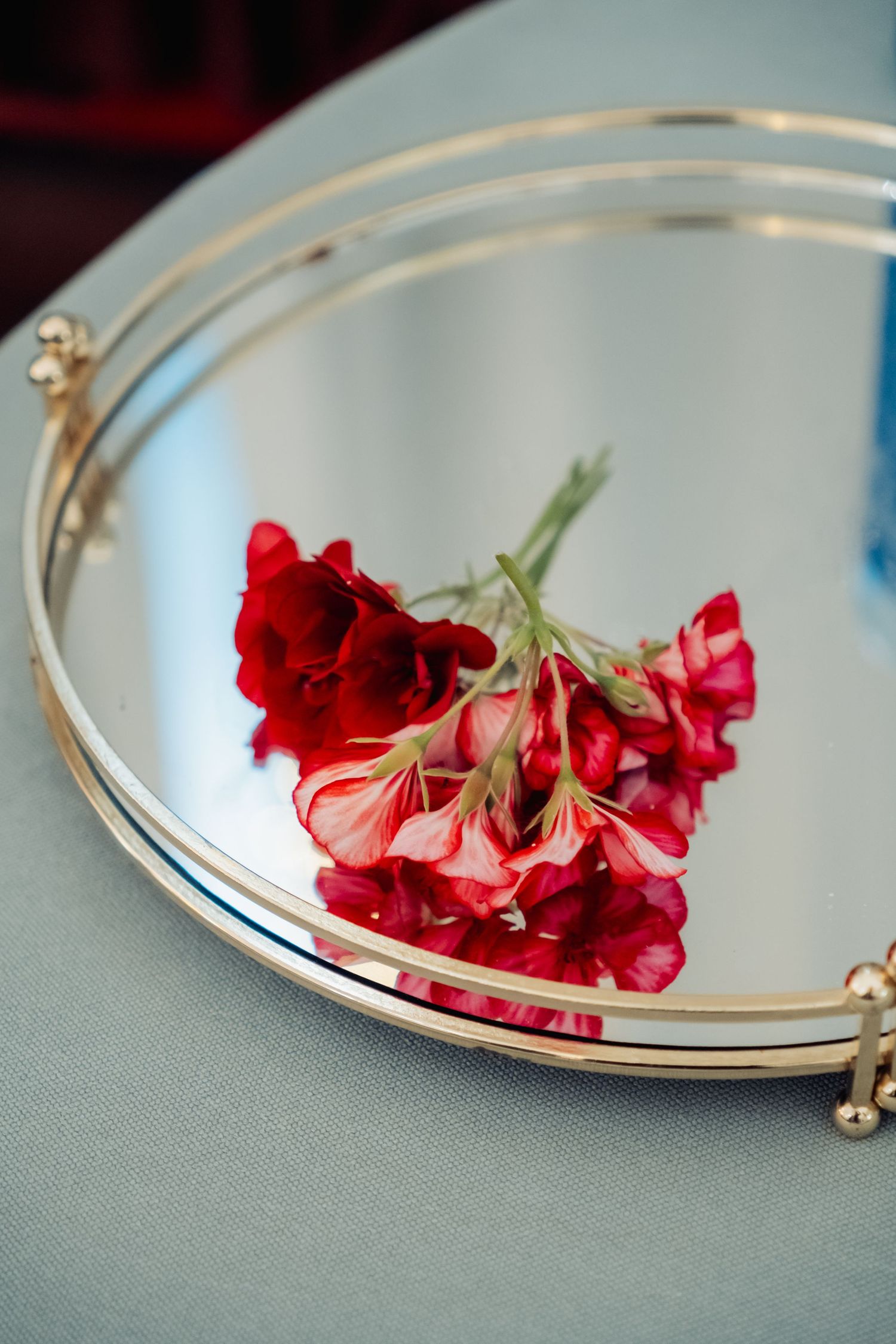 Red geranium flowers resting on a gold-framed mirrored tray at a wedding reception.