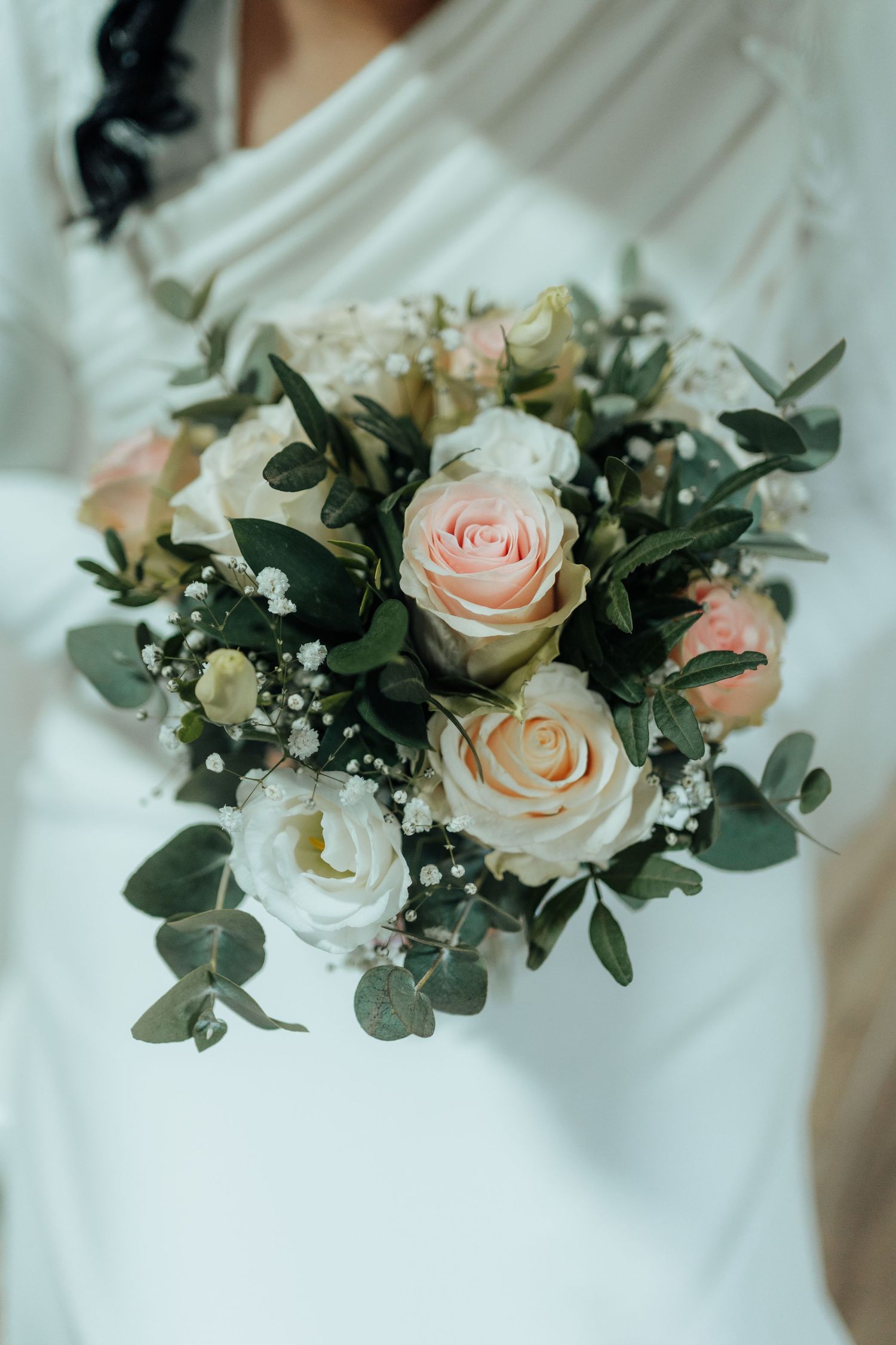 Bride in white gown holding elegant bouquet of pink and white roses with eucalyptus and baby's breath.
