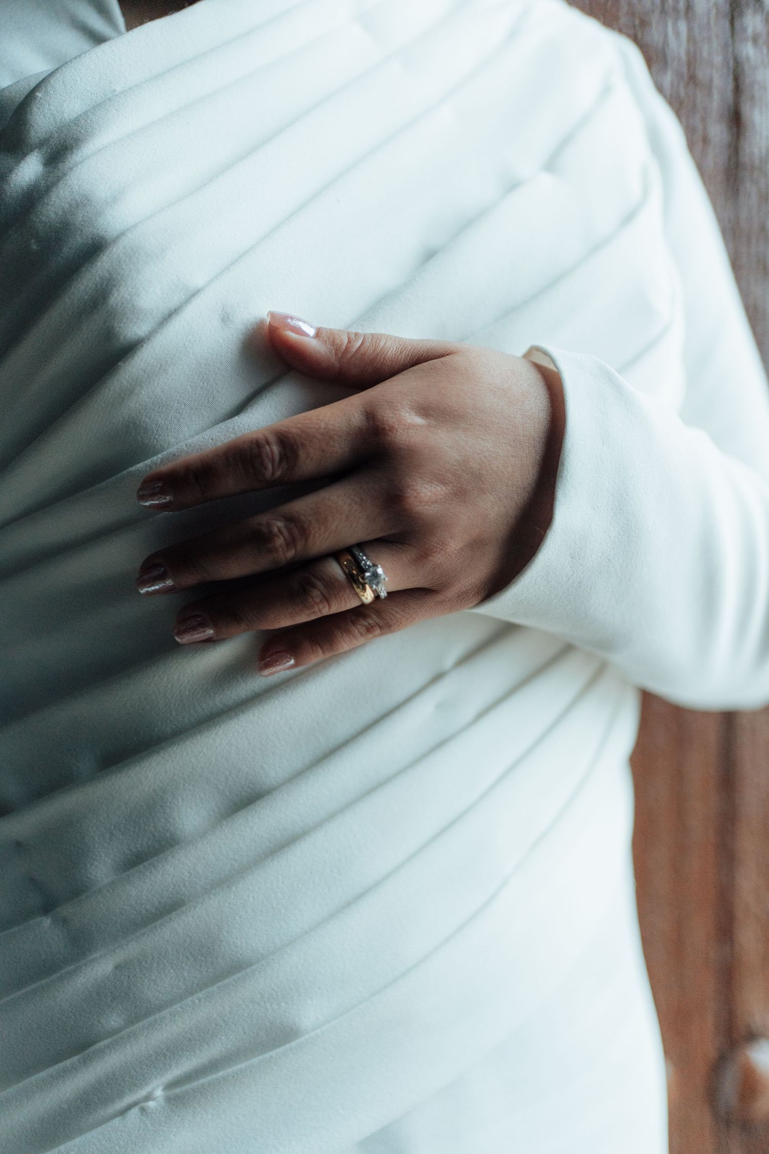 Close-up of a bride's hand with a stunning ring resting on her white pleated wedding dress.