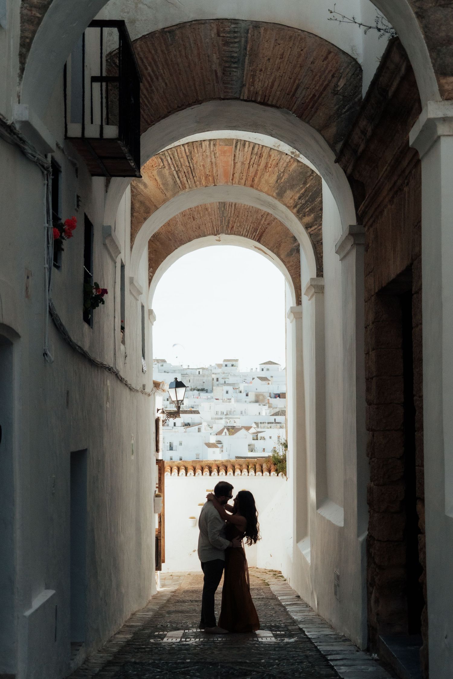 Couple silhouetted kissing under white arched tunnel in Vejer de la Frontera, Spain.