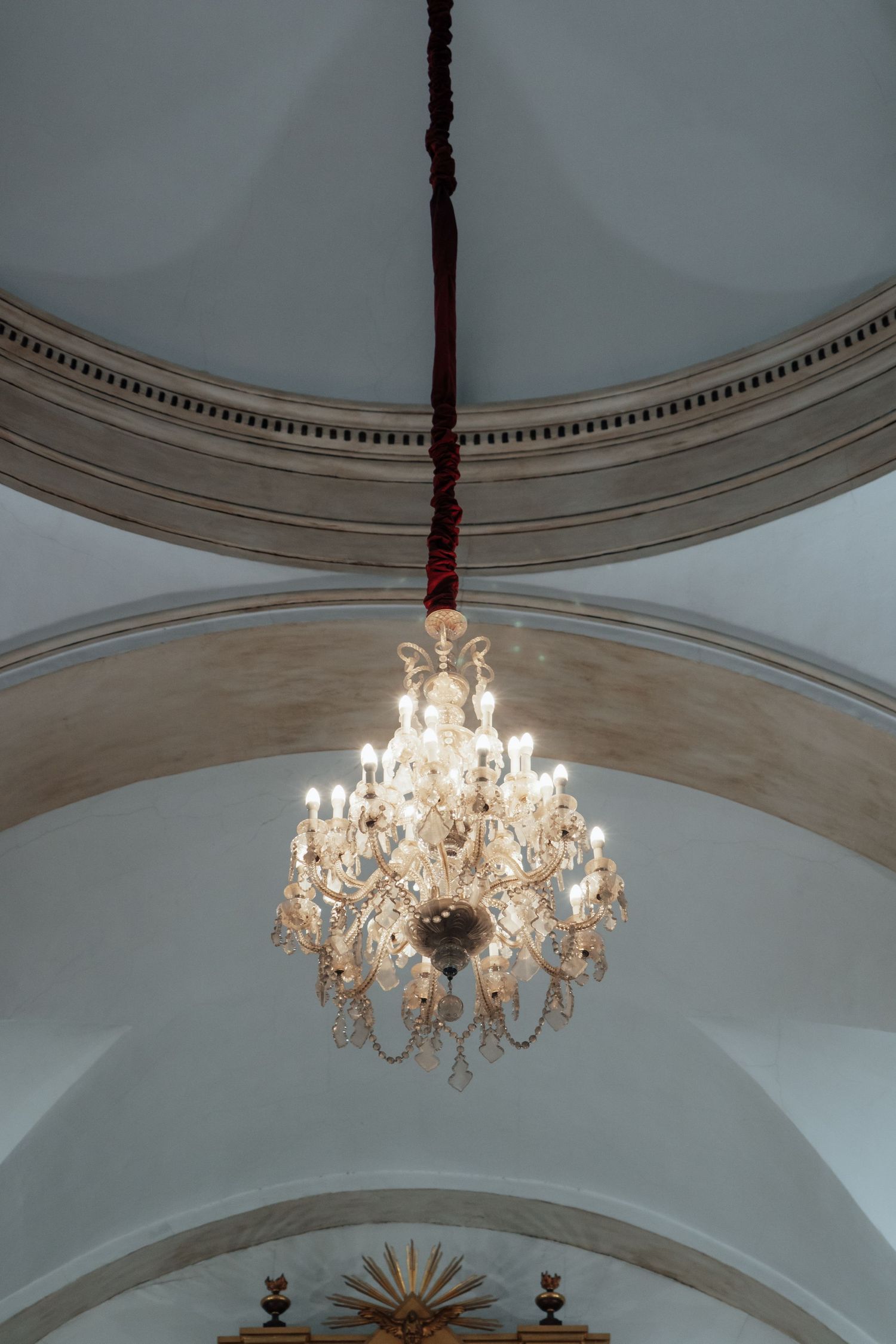 Crystal chandelier hanging from arched ceiling in a historic Catholic church interior.