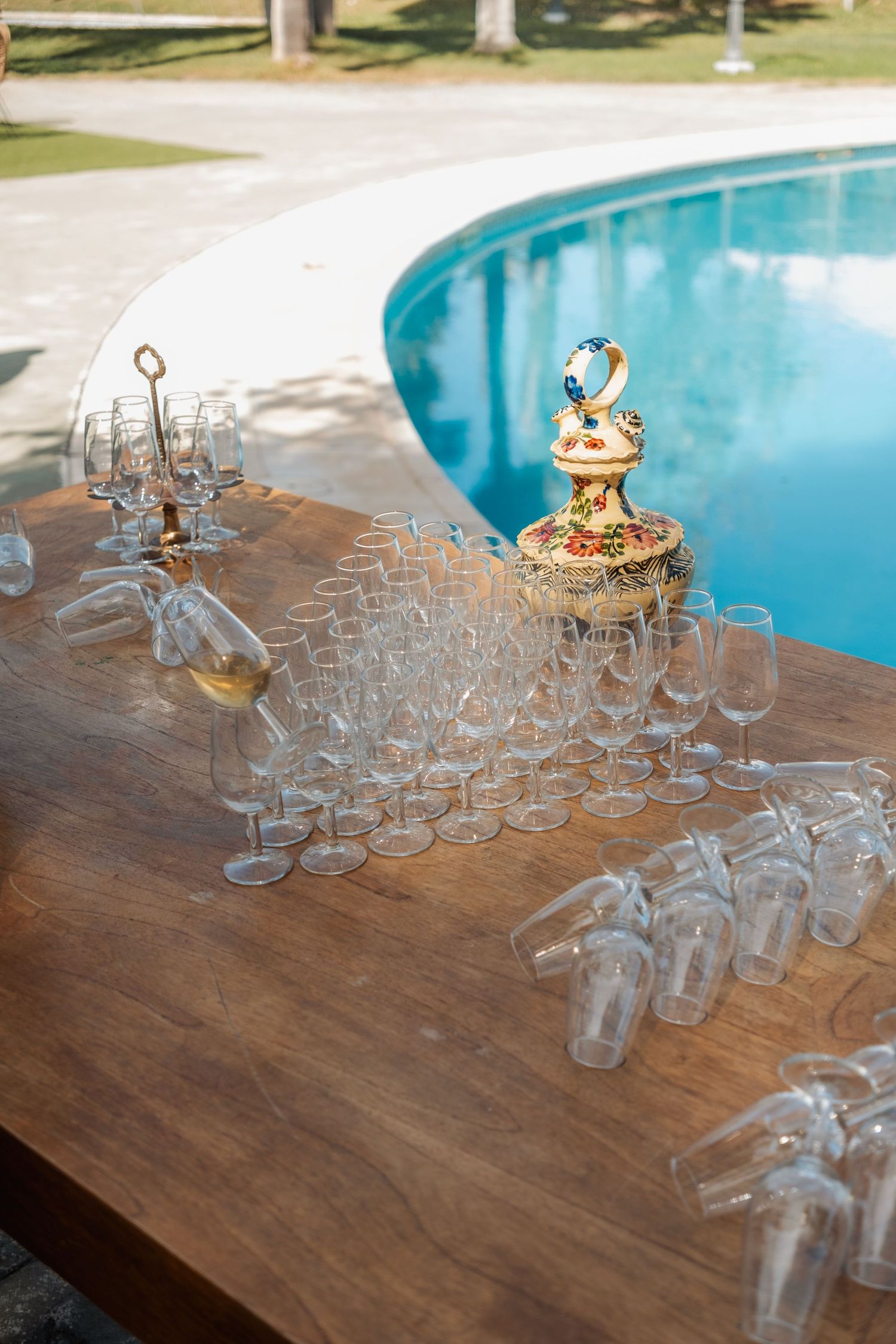 Elegant outdoor bar setup with rows of champagne glasses on a wooden table beside a pool.