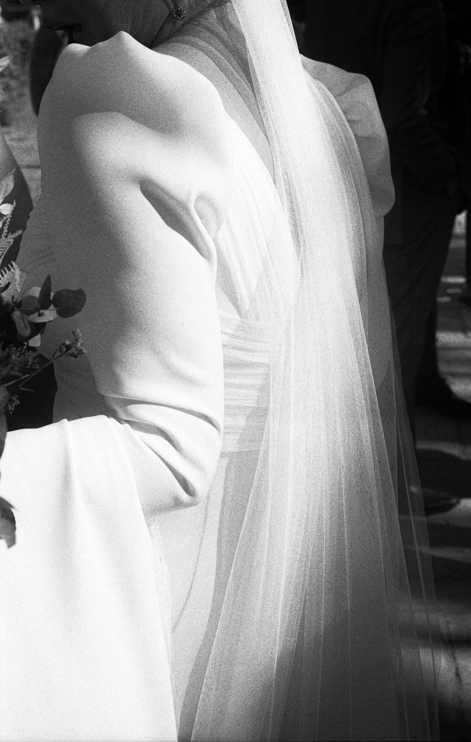 Close-up of bride in white sleeveless gown with flowing veil, elegant black and white wedding photo.