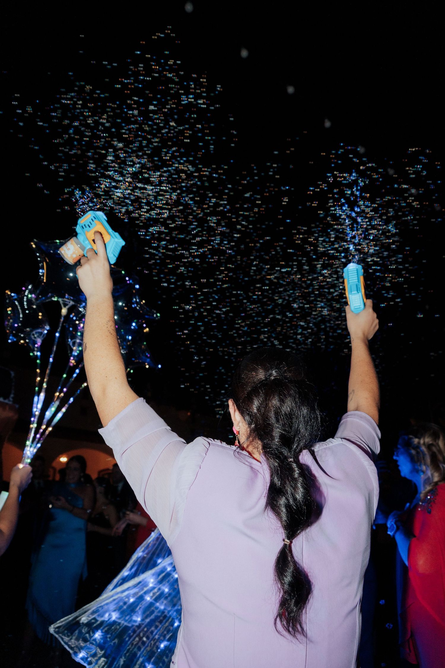 Woman shooting confetti cannons into the air at a festive nighttime outdoor party celebration.