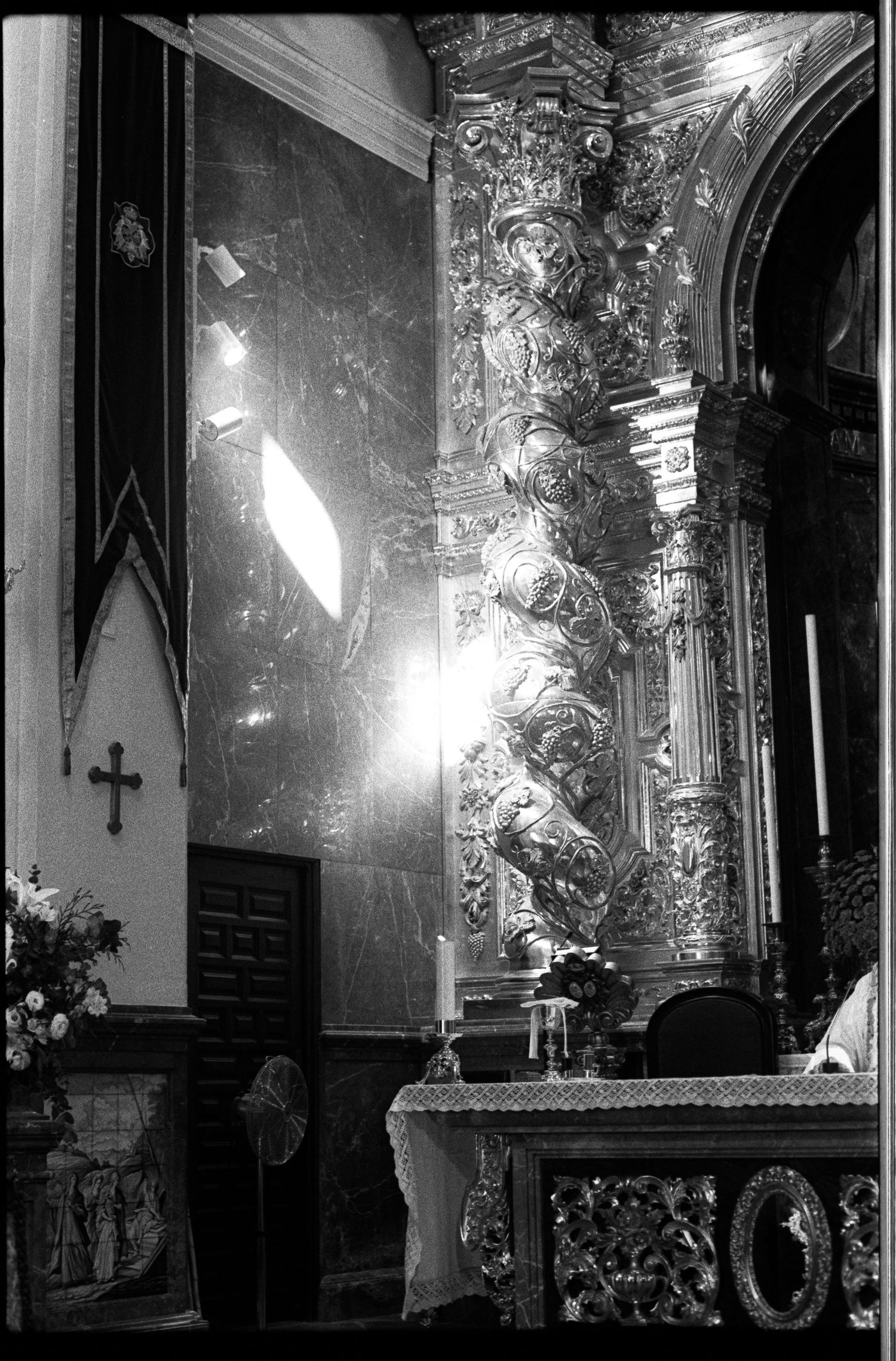 Black and white photo of ornate church altar with gilded baroque column, candles, and cross during wedding ceremony.