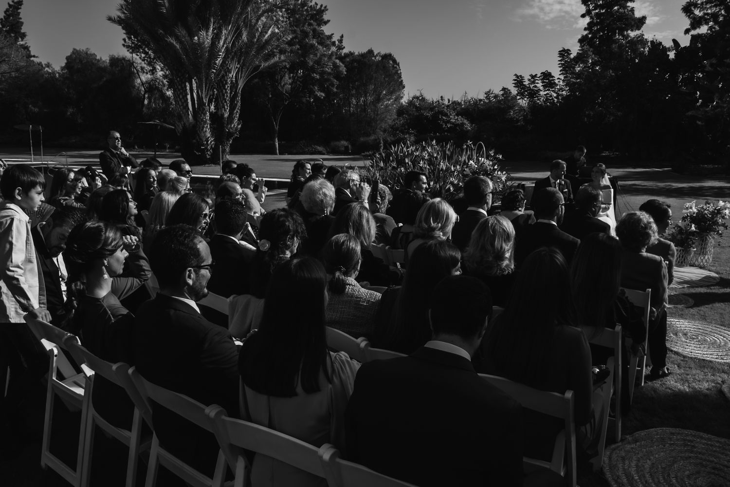 Black and white photo of wedding guests seated in rows at outdoor garden ceremony.