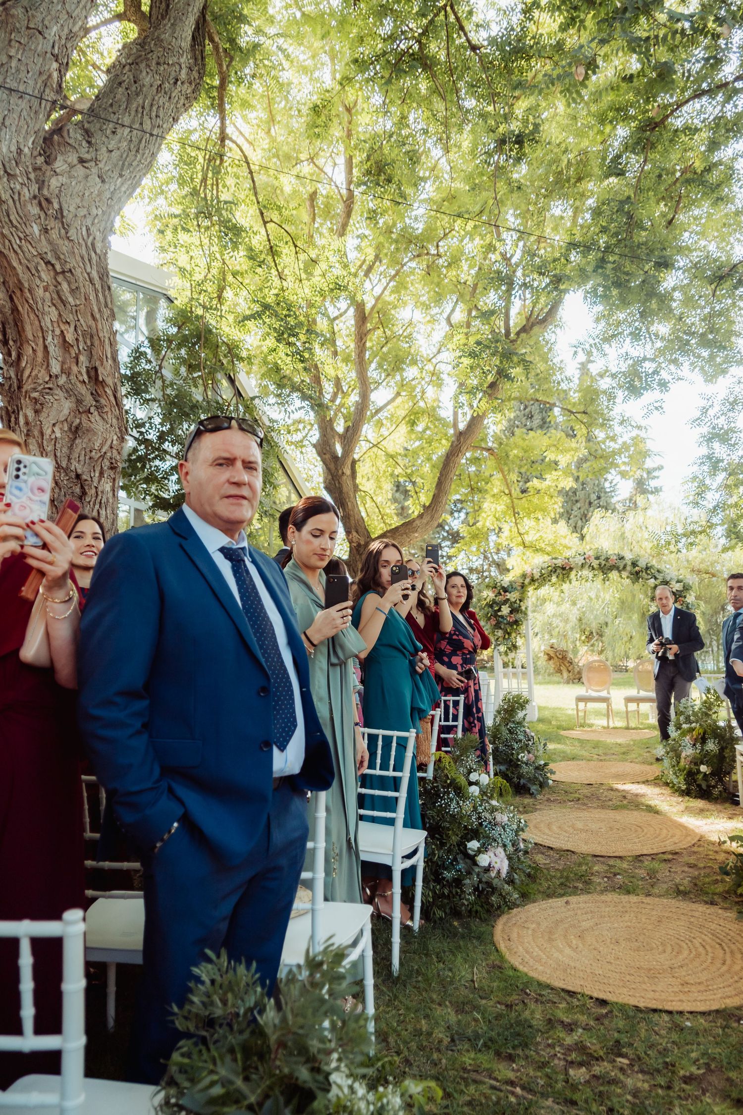 Wedding guests stand along the aisle watching the bride's processional at an outdoor ceremony.