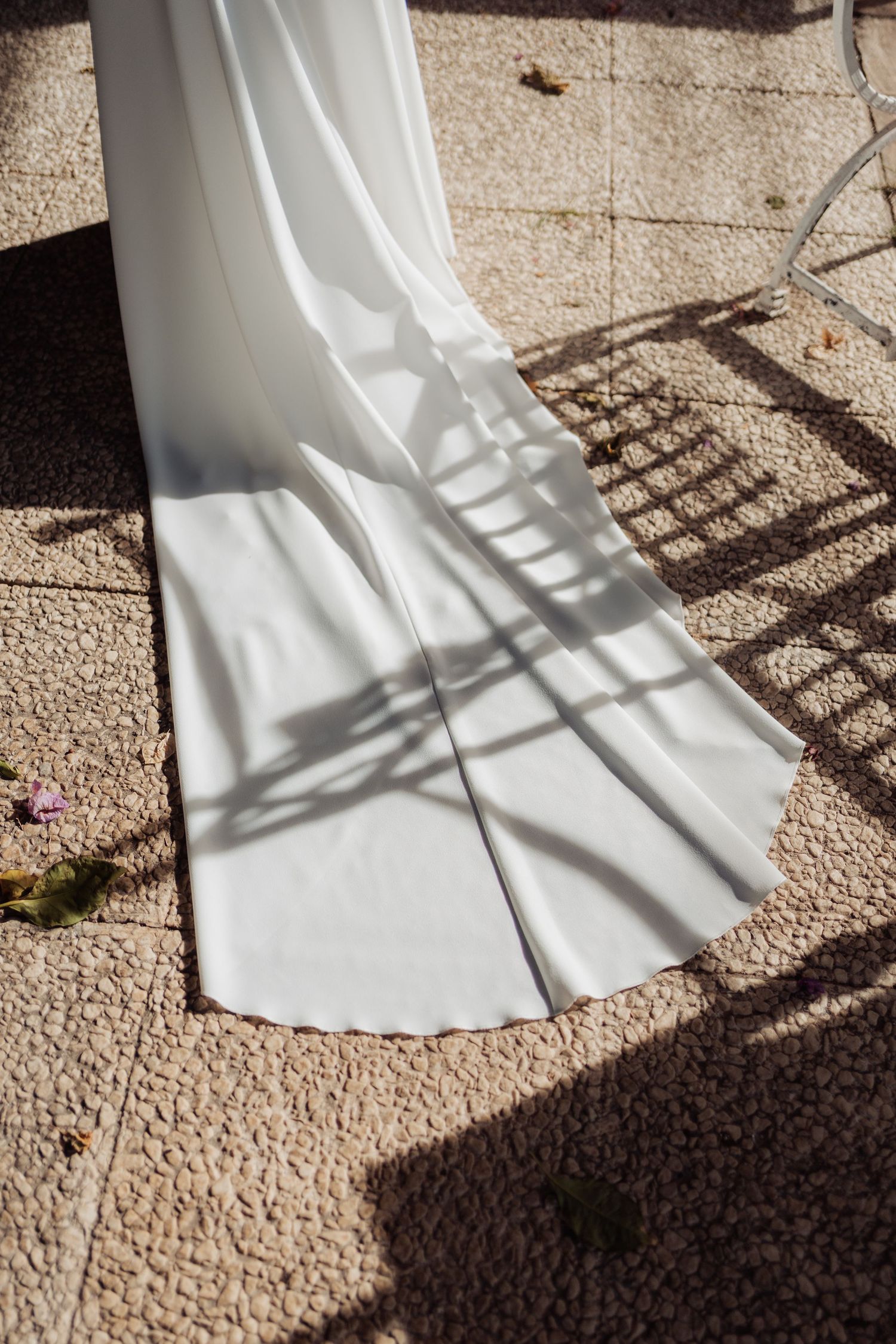 White wedding dress train casting elegant shadows on stone patio in sunlight.