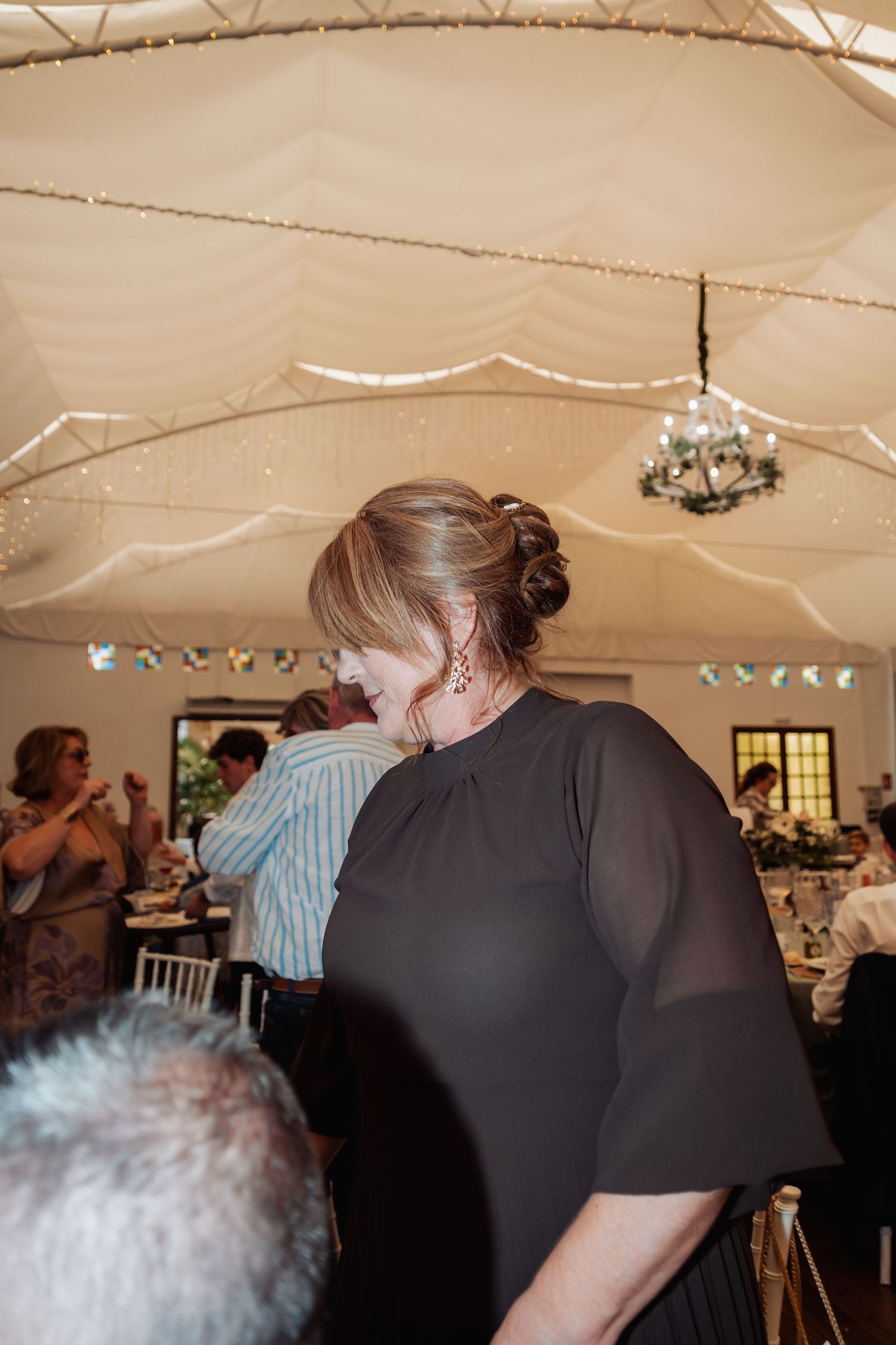 Woman in black dress smiling and laughing at an elegant wedding reception under a draped ceiling.