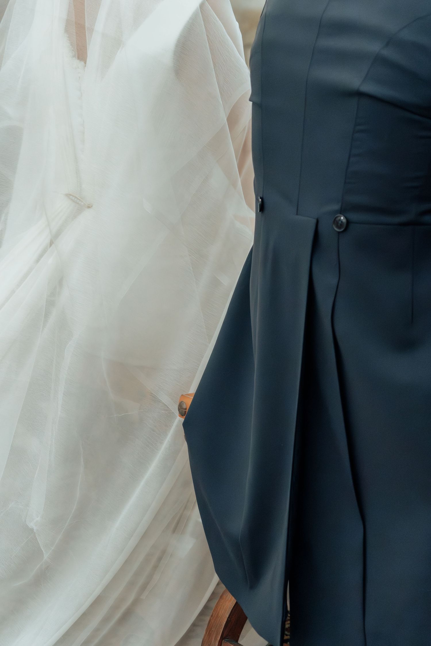 Close-up of bride in white gown standing beside person in dark teal pleated dress at wedding.