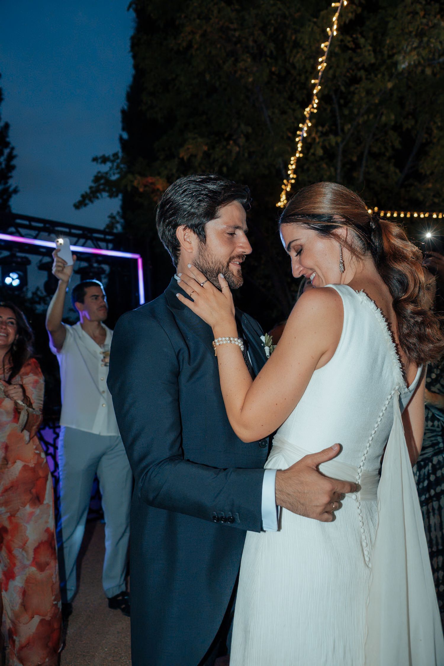 Bride and groom share an intimate dance moment at outdoor evening wedding reception with string lights.