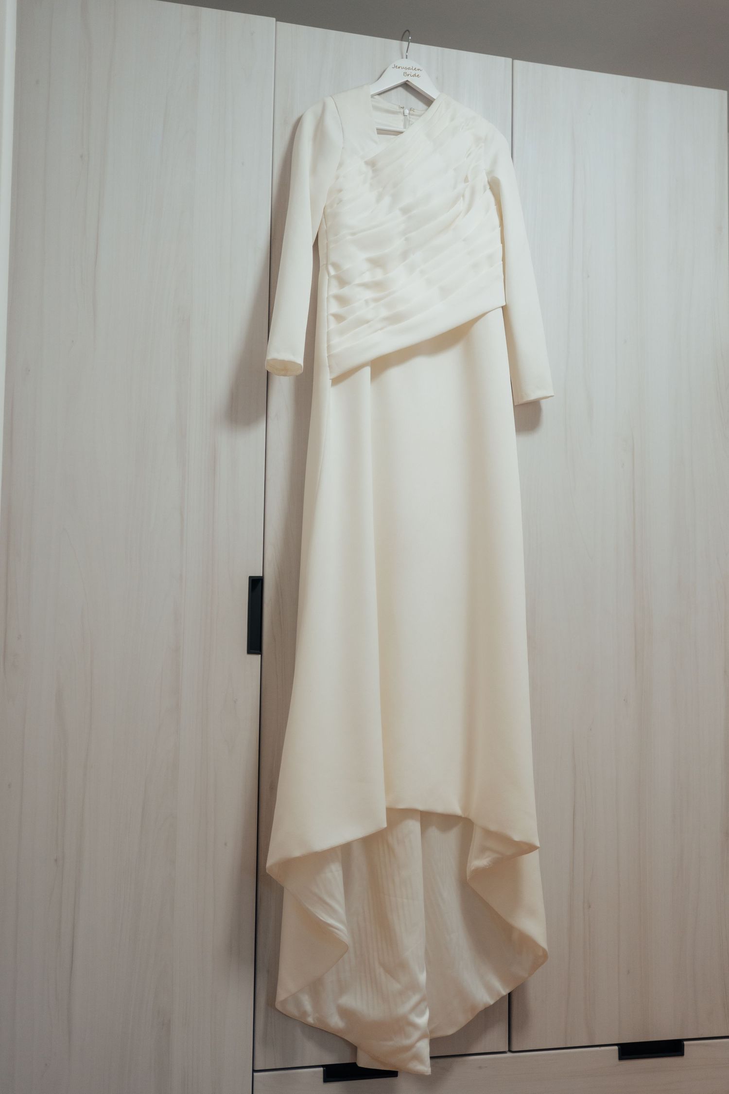 An elegant long-sleeve ivory wedding dress hangs on a wooden wardrobe before the ceremony.
