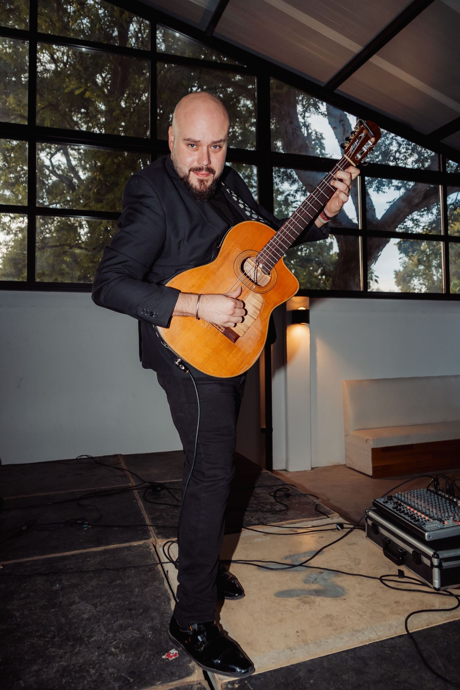 Bald guitarist in black suit passionately playing acoustic guitar on stage at an elegant wedding venue.