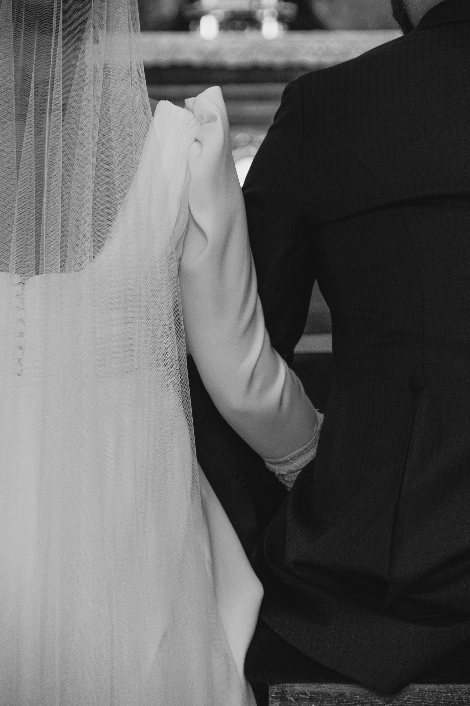 Black and white photo of bride and groom holding hands at church altar during wedding ceremony.