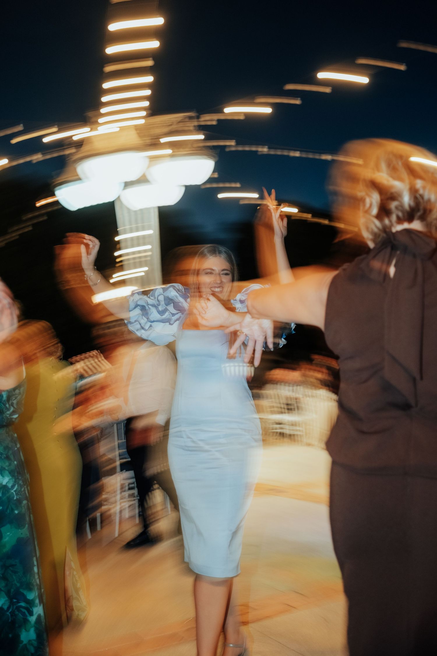 Woman in light blue dress dancing joyfully at wedding reception with motion blur effect.