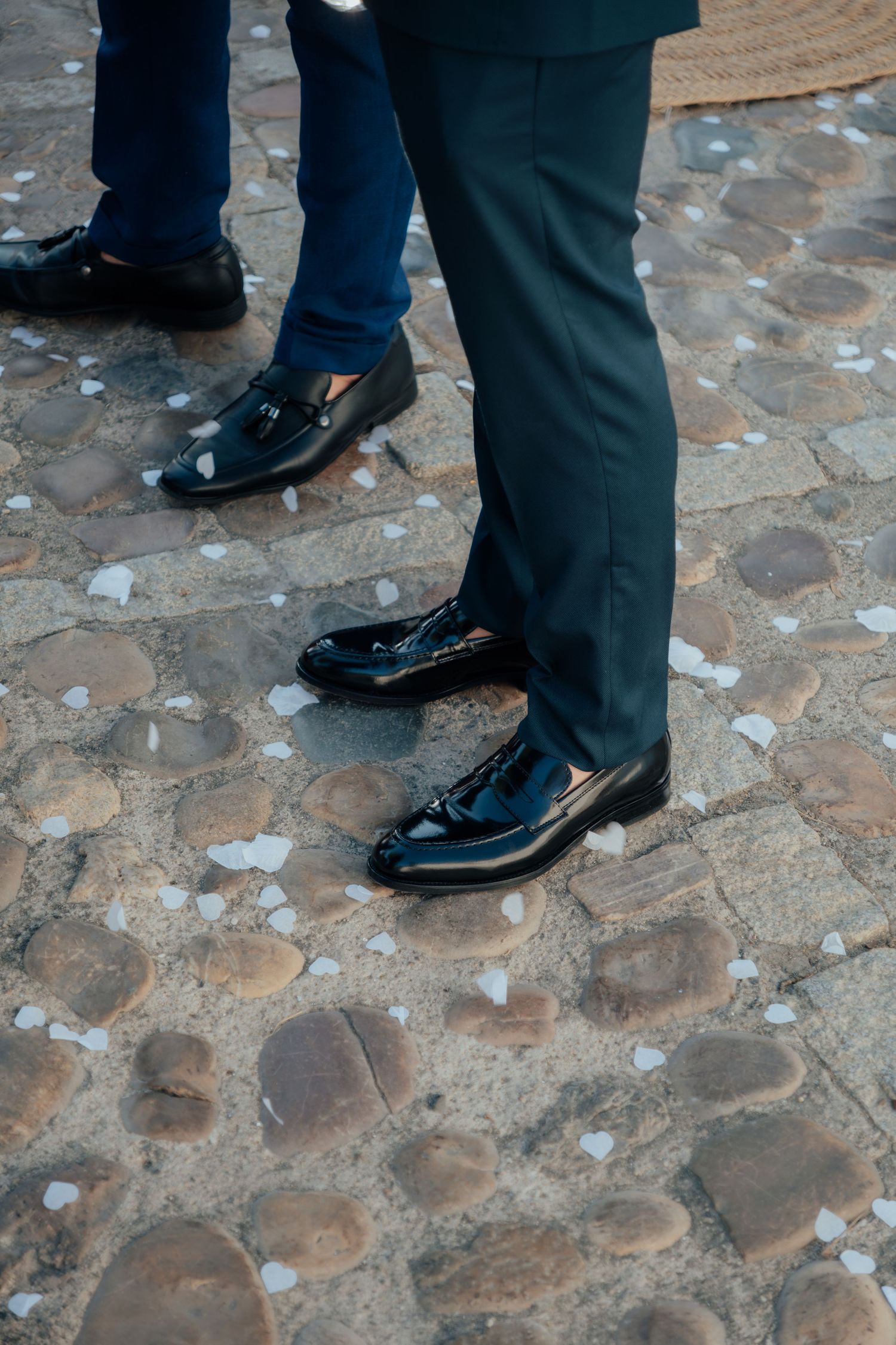 Close-up of mens polished black patent leather dress shoes on cobblestone wedding venue floor.