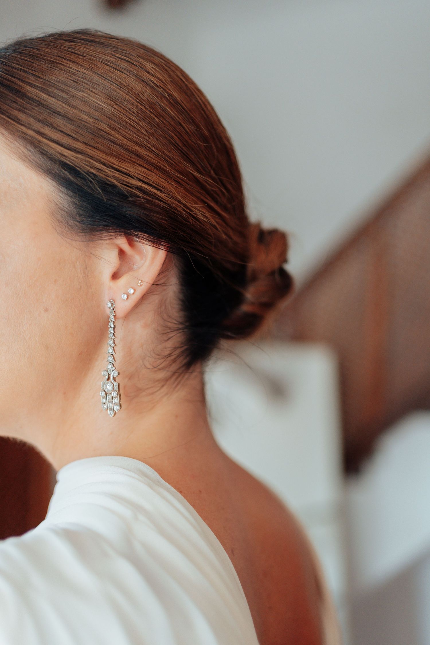 Close-up of bride with elegant updo wearing sparkling diamond drop earring on wedding day.