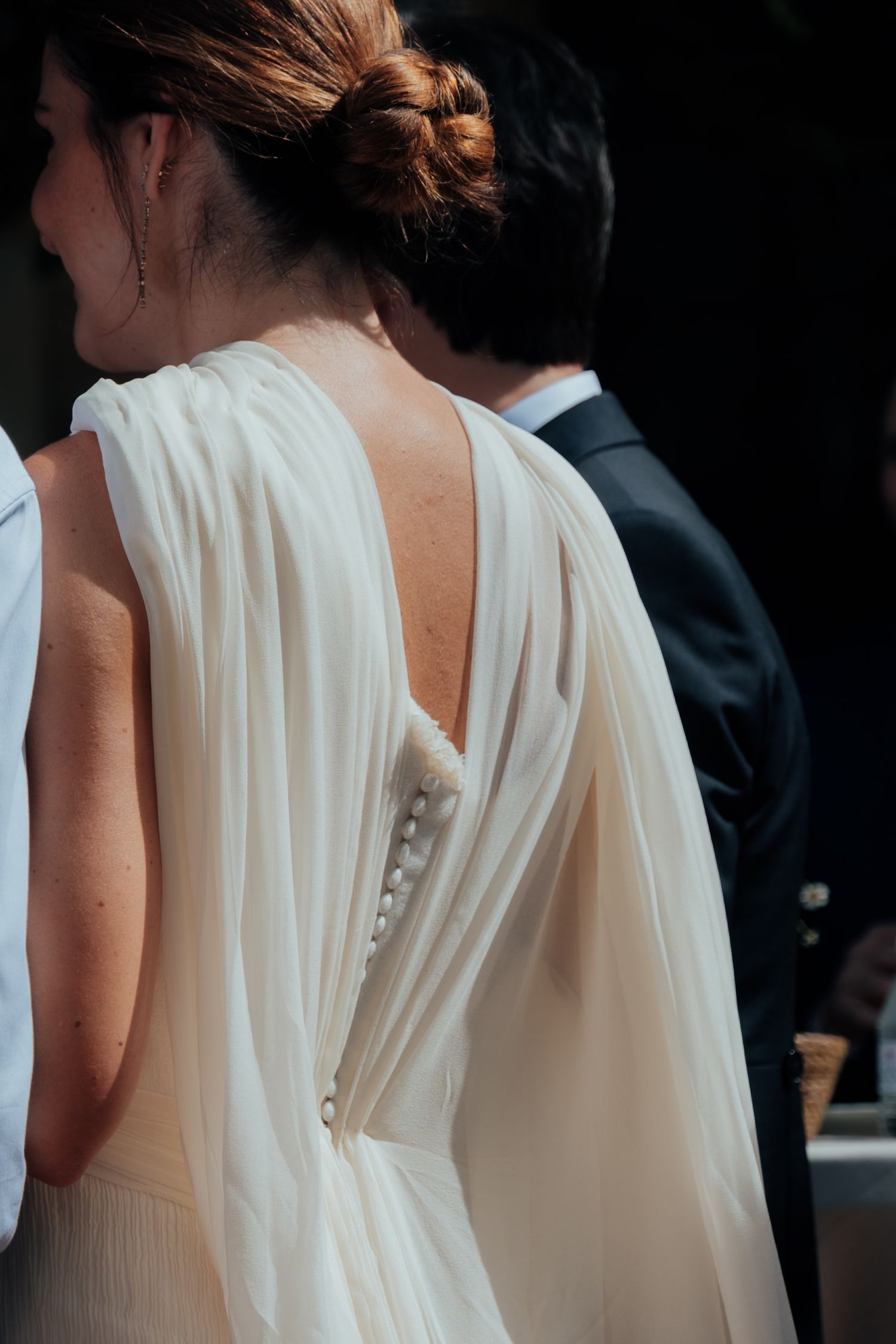 Close-up of bride's elegant white chiffon wedding dress with pearl button back detail and updo.