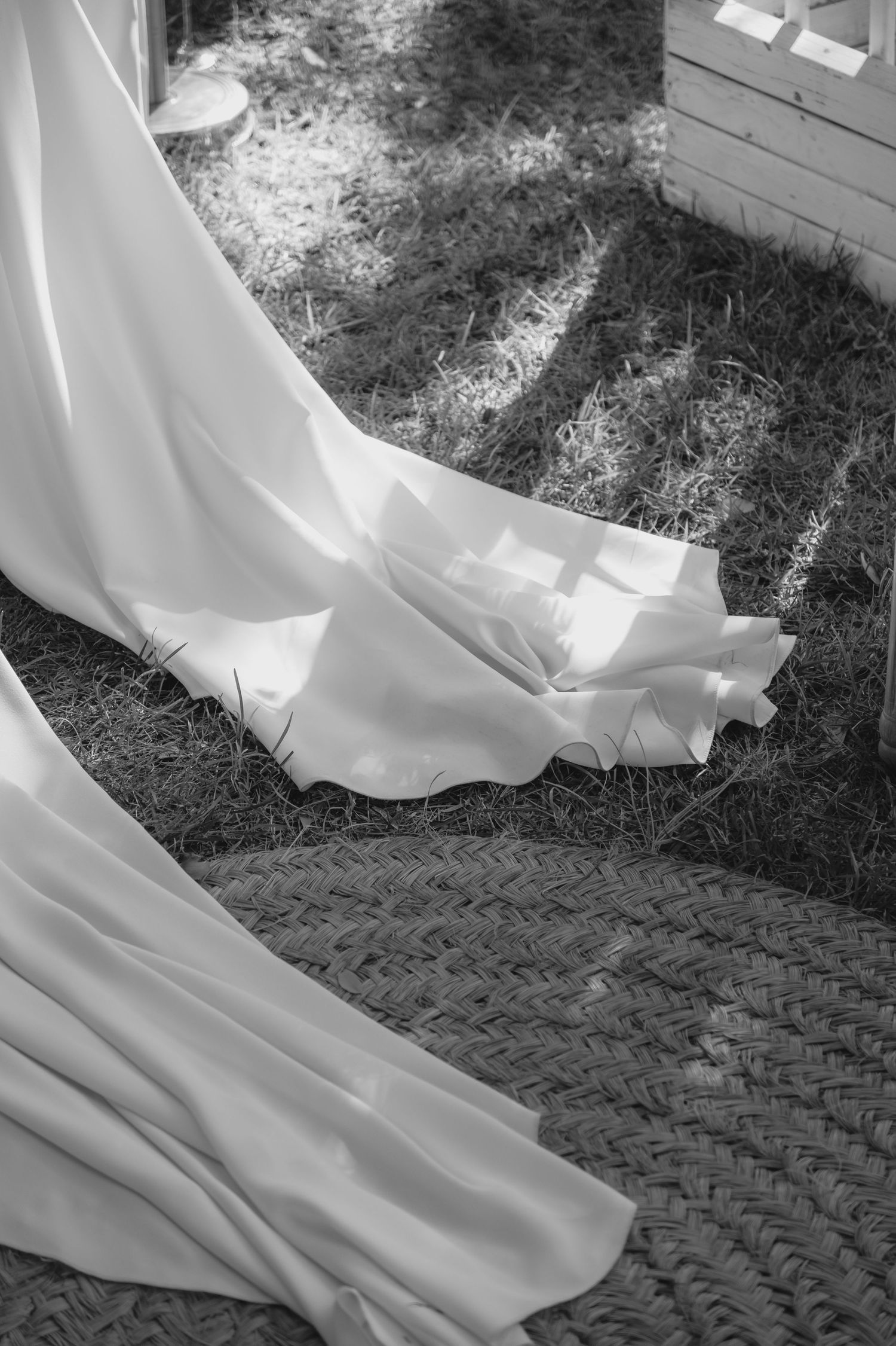 Black and white close-up of elegant white bridal gown train on grass at outdoor wedding.