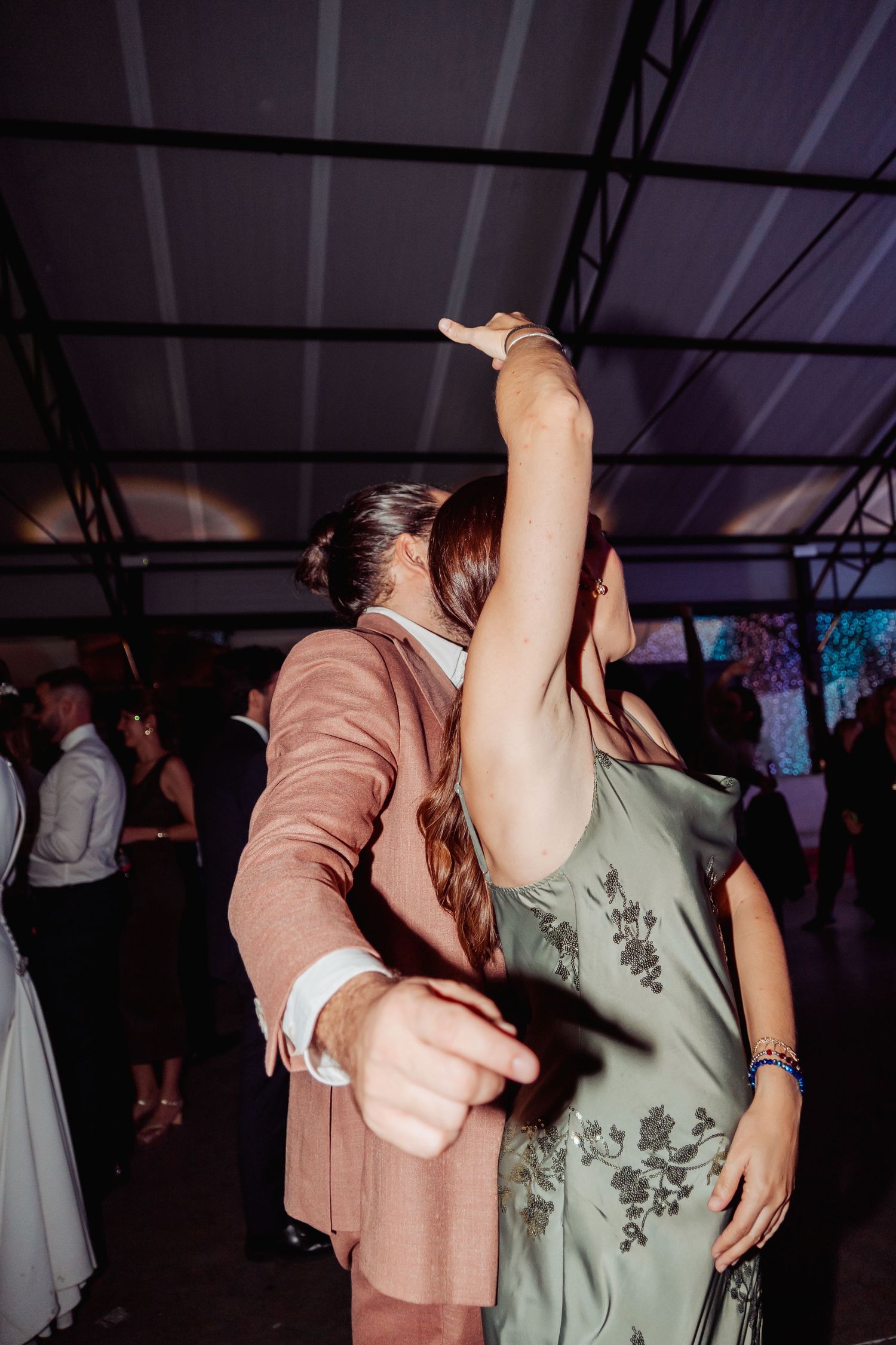 Couple dancing together at a wedding reception, woman in green floral dress raises arm elegantly.