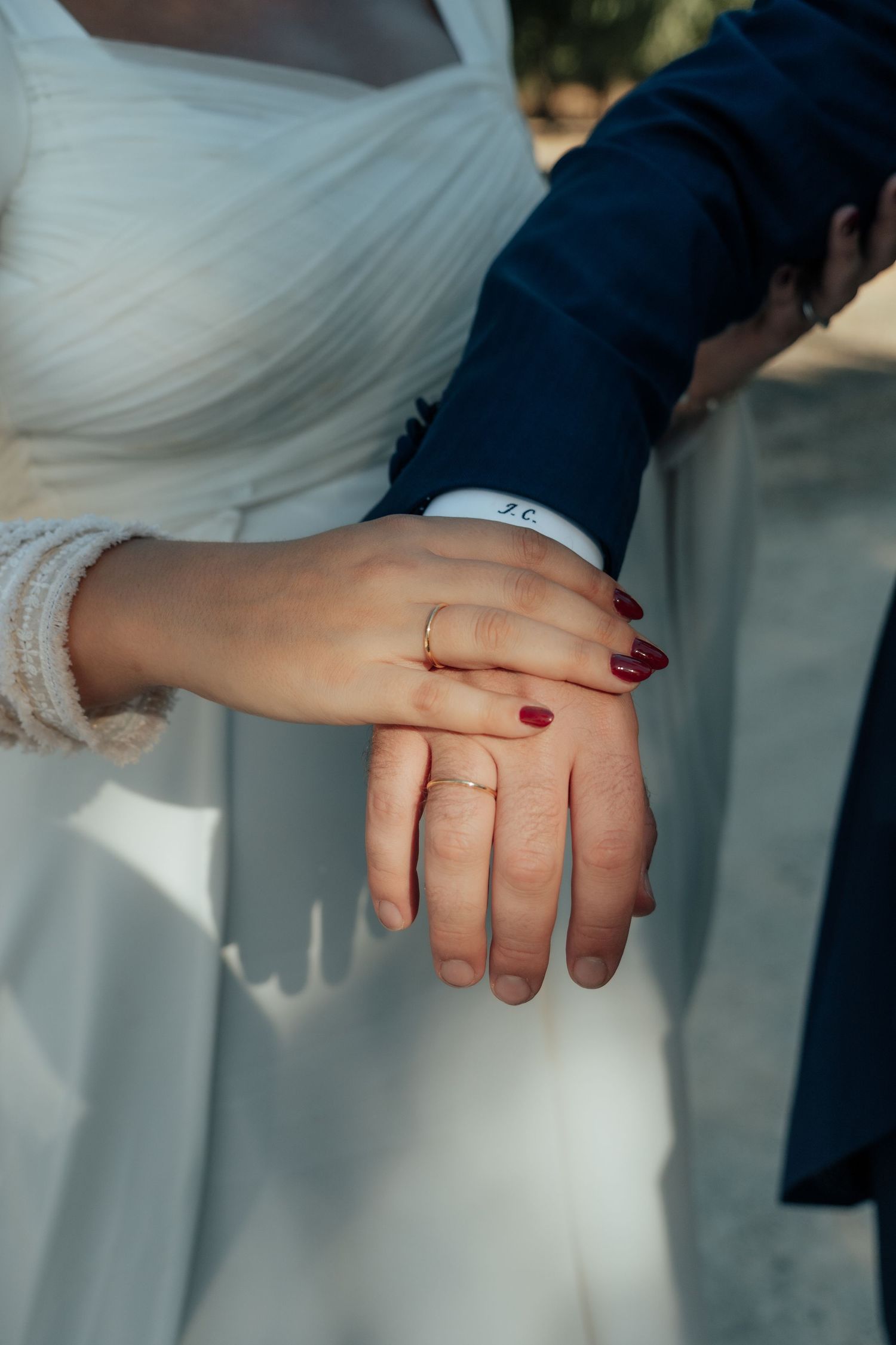 Close-up of bride and groom's hands showing wedding rings, bride with red nail polish.