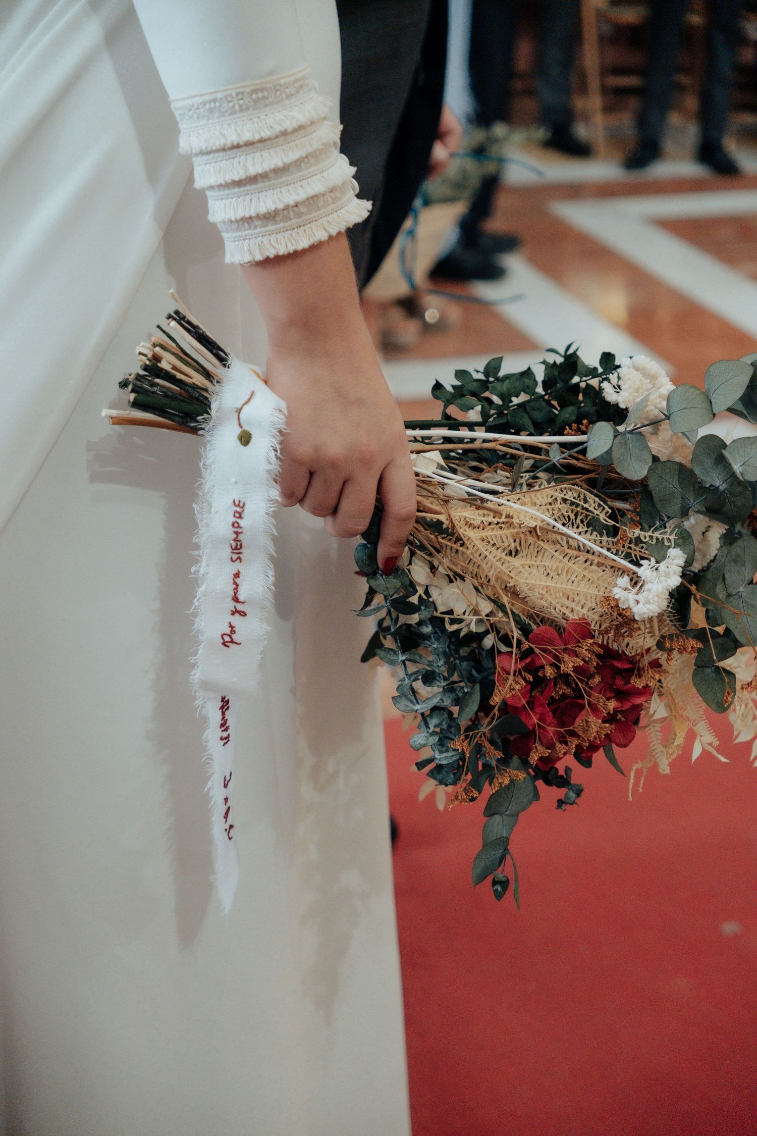 Bride holding rustic dried flower bouquet with white ribbon inside decorated church.