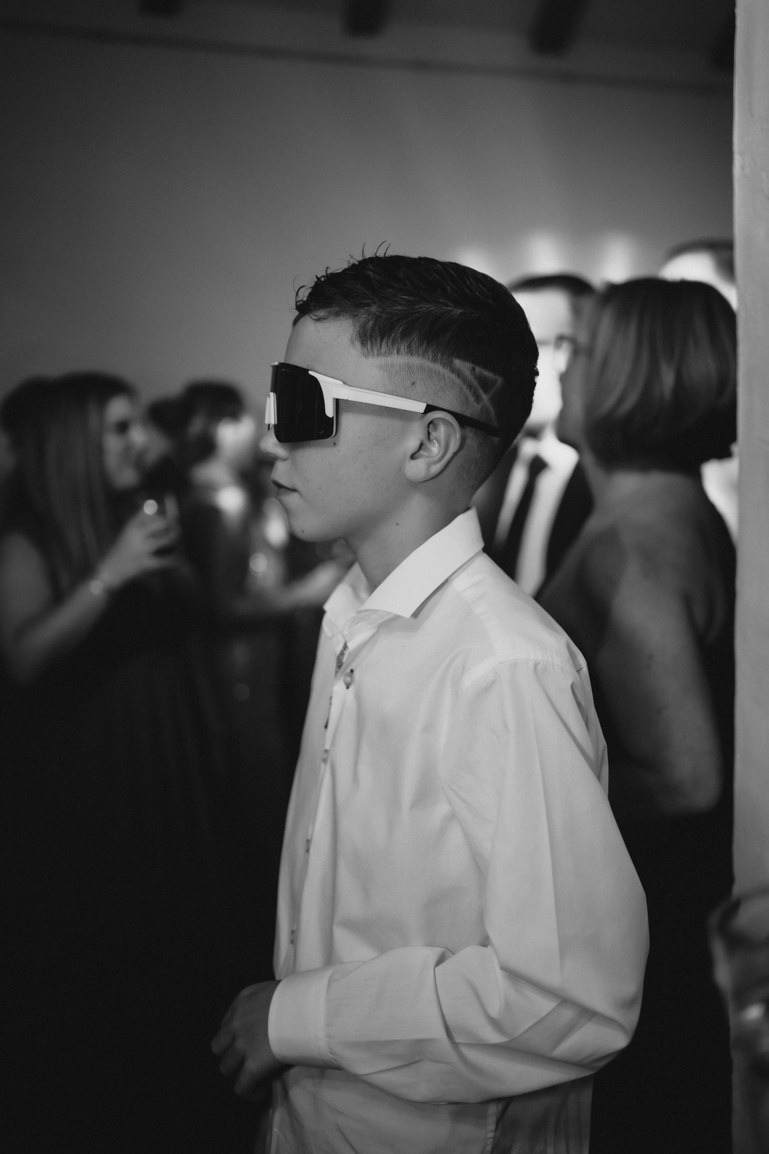 Stylish young boy wearing oversized white sunglasses in black and white photo at a formal event.