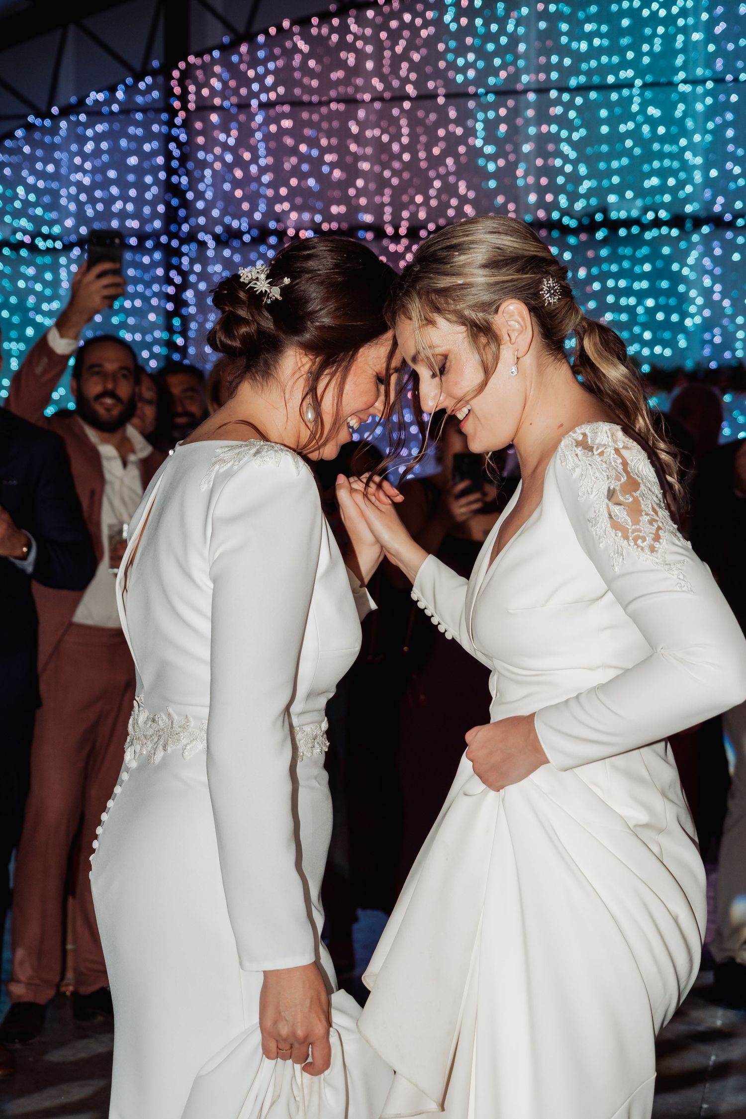 Two brides in white wedding gowns sharing an intimate moment together on the dance floor at their wedding.