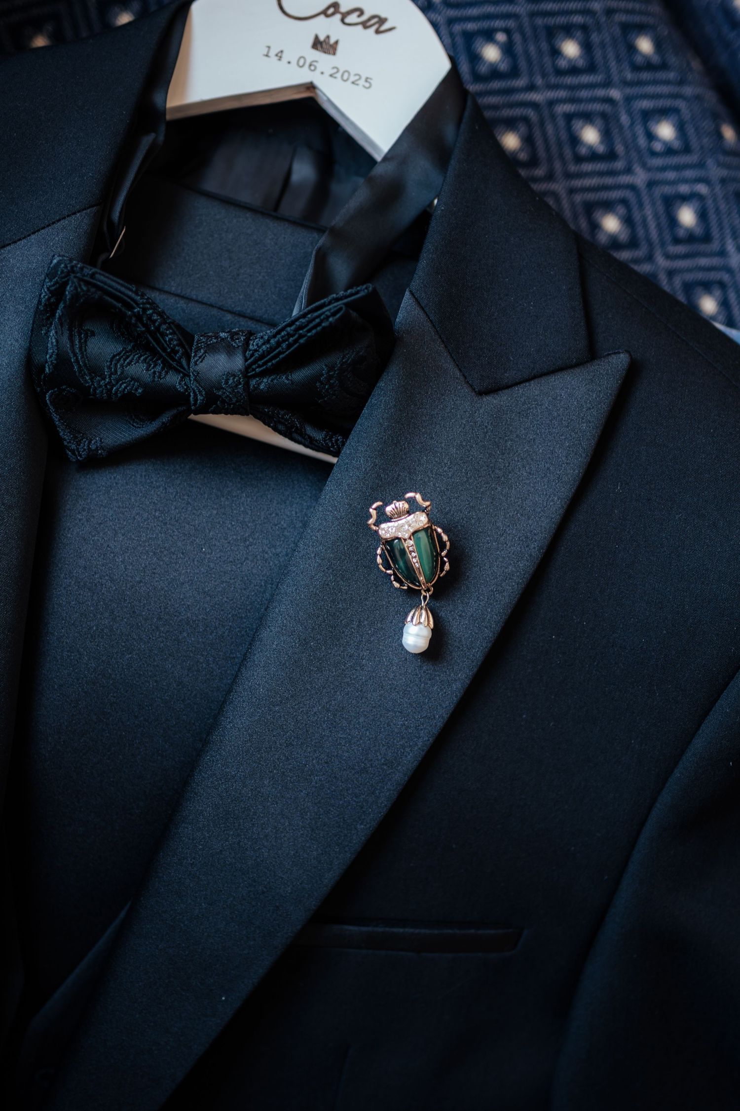 Black tuxedo jacket with bow tie and decorative cactus lapel pin on hanger.