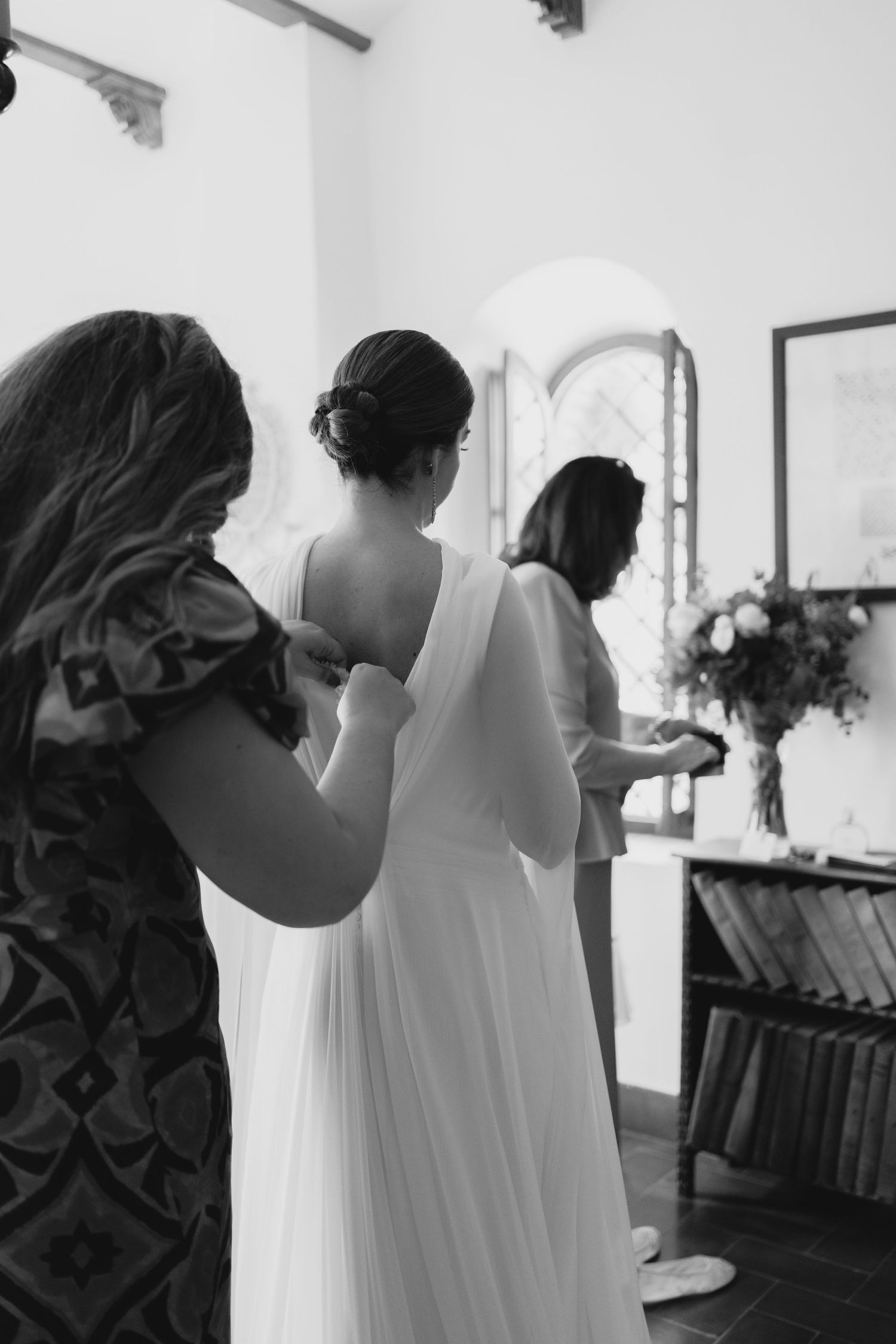 Black and white photo of bridesmaids helping bride fasten her white wedding gown.