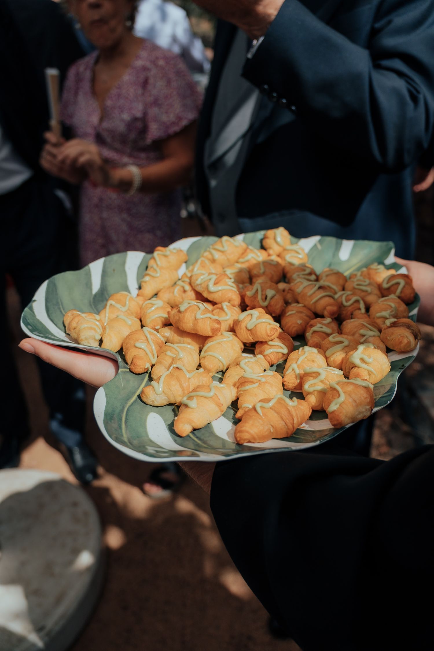 Server holding decorative leaf-shaped platter of fresh mini croissants at catered event.