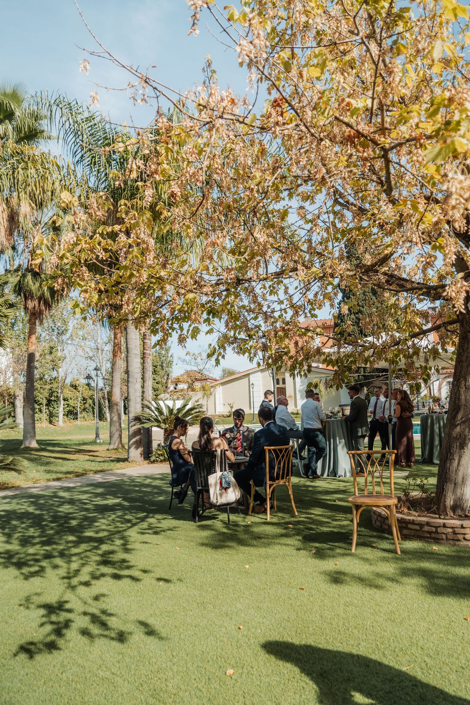 Wedding guests gathered under autumn trees in a lush garden venue.
