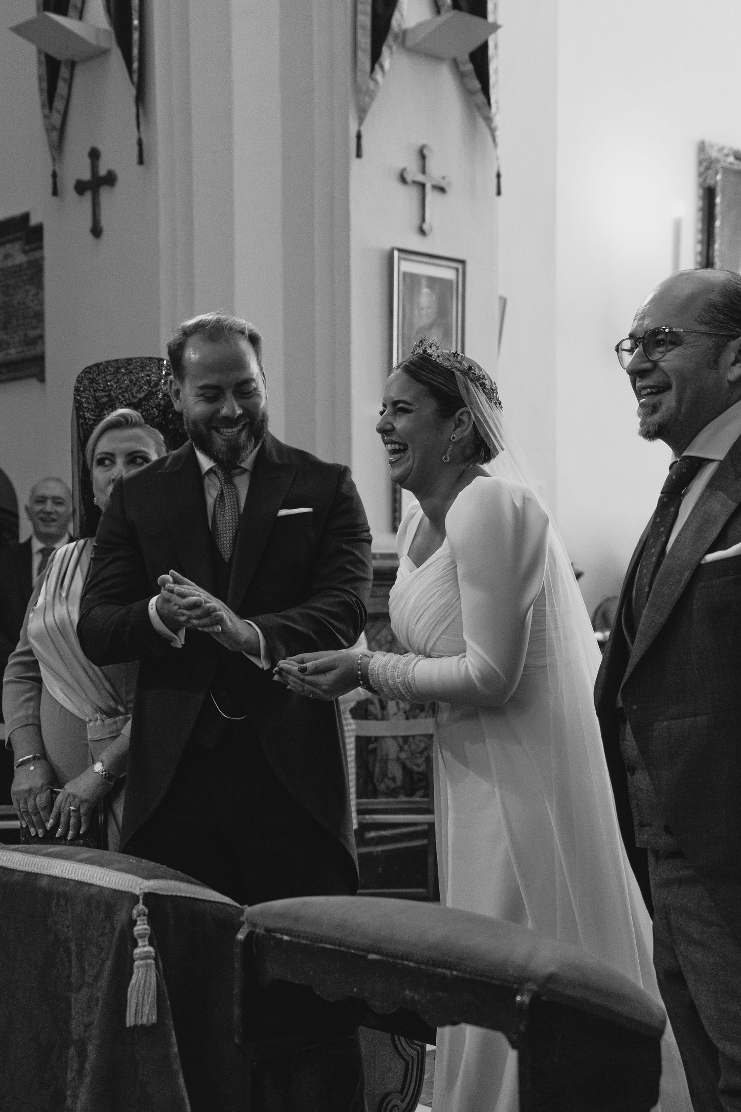 Black and white photo of laughing bride and groom exchanging rings during joyful church wedding ceremony.