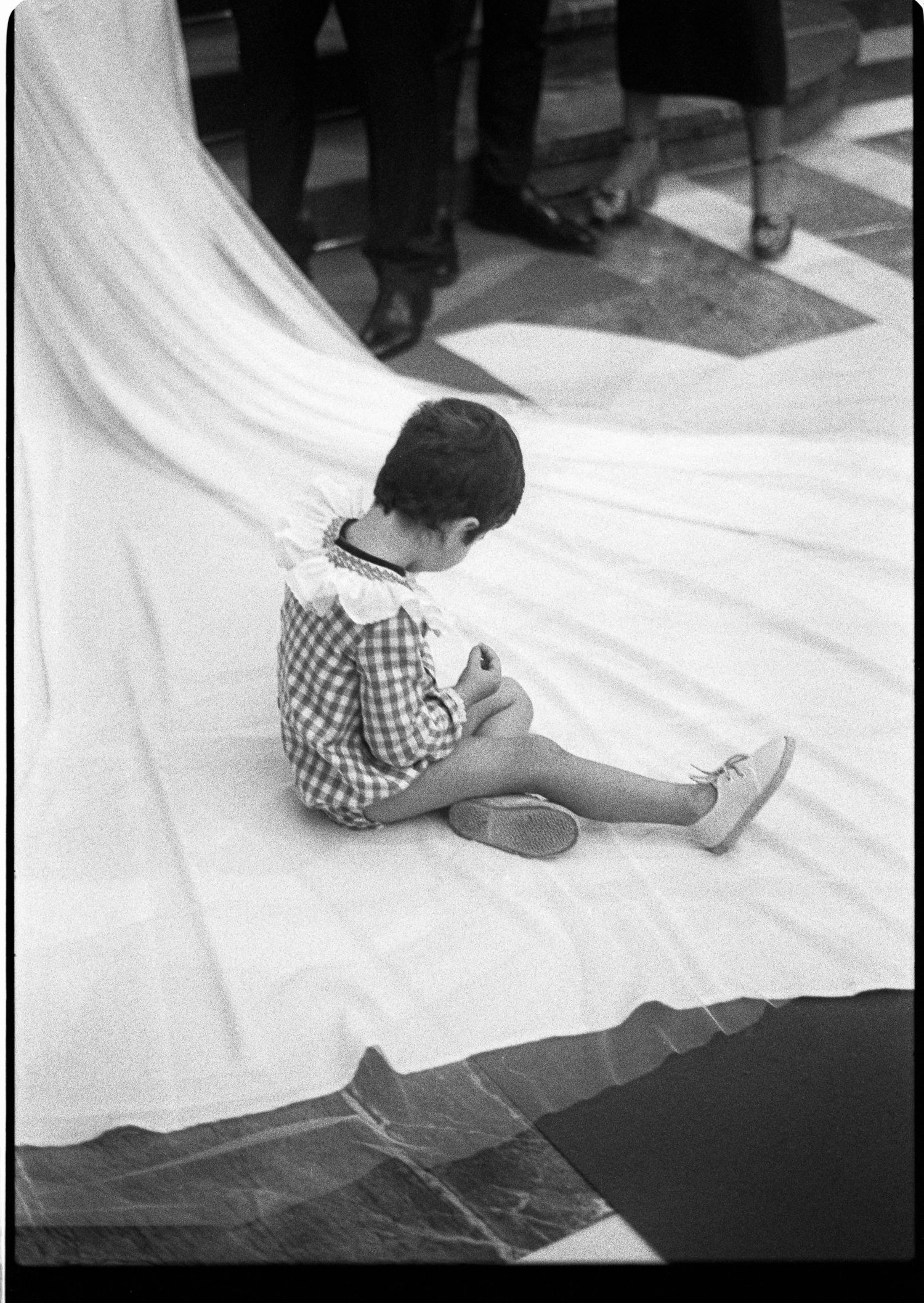 Small child sitting on bride's white wedding dress train on church floor.