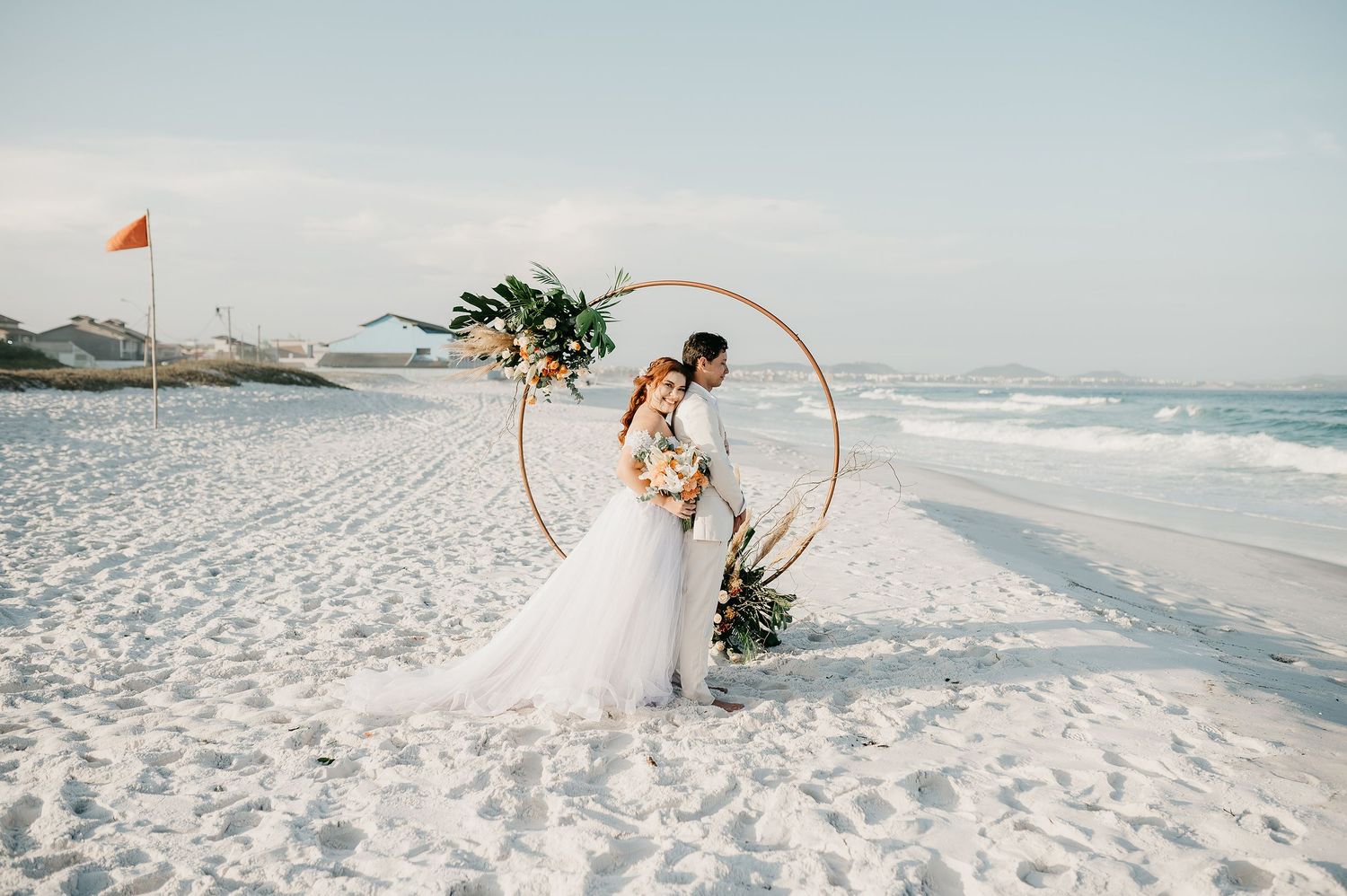 Cerimônia de casamento a dois ao pôr do sol na Praia do pontal, Arraial do Cabo. Casal no altar com arco floral.