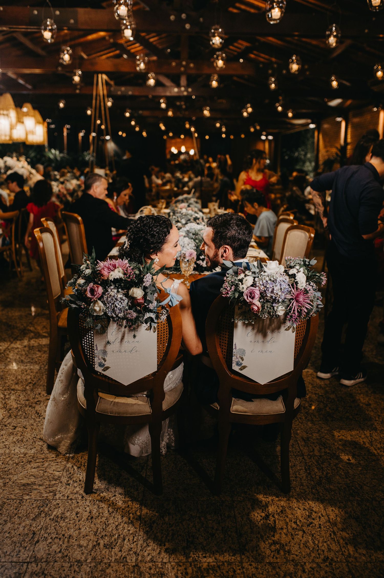 Mesa dos noivos Raquel e David com iluminação suspensa e flores. Decoração de casamento noturno rústico-chique no Vale dos Sonhos.