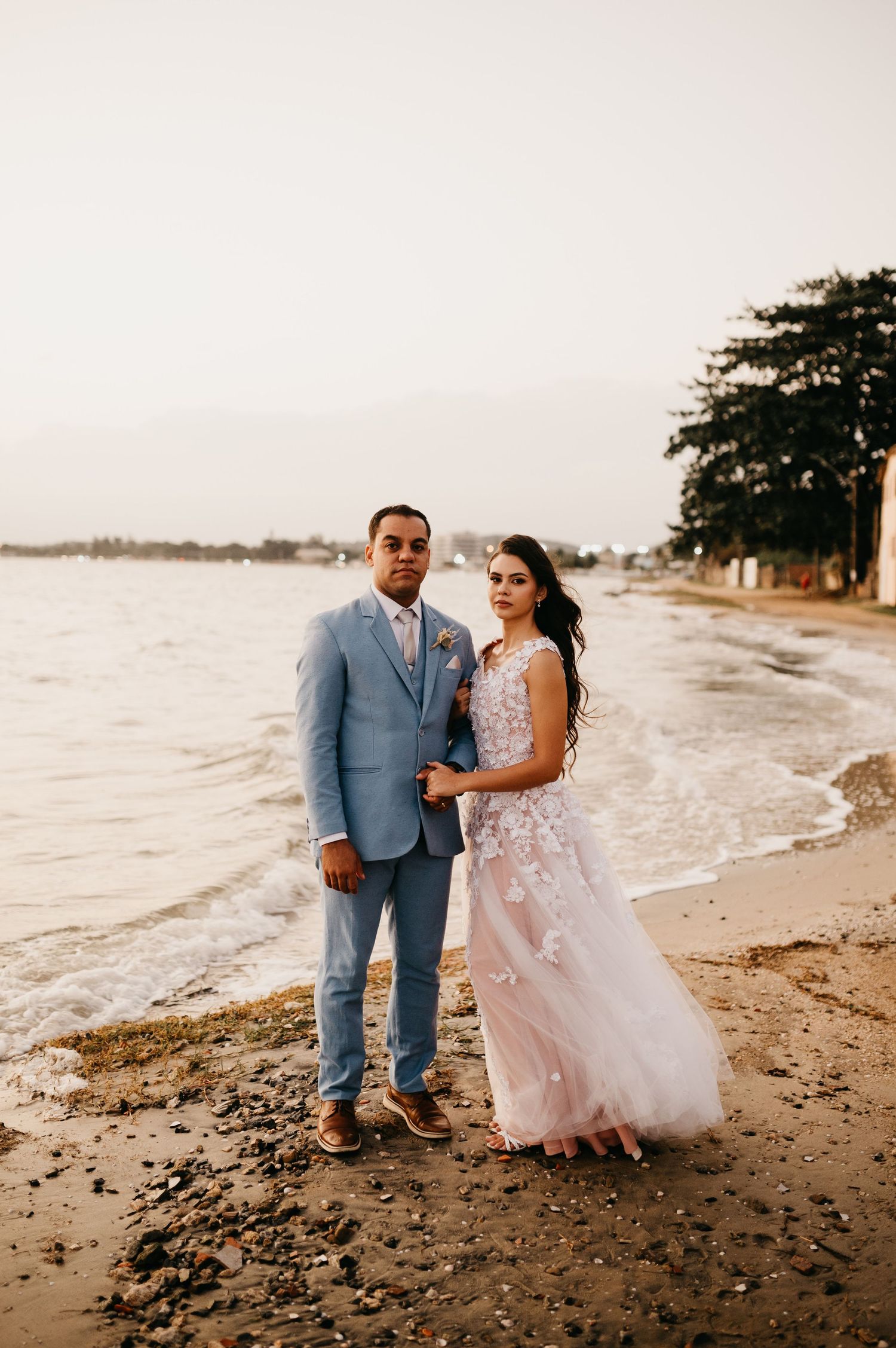 Casal de noivos, Ana e Jhon, em pé na beira da Lagoa de Araruama em São Pedro da Aldeia ao entardecer.