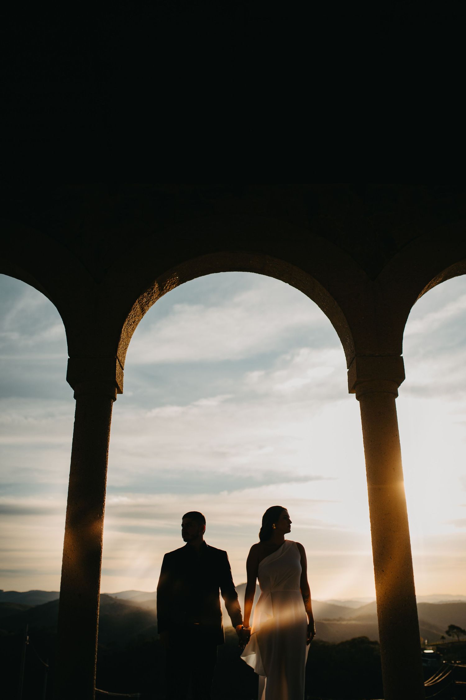 Casal de mãos dadas sob os arcos de pedra do Borgo del Vino, em Areal, durante o pôr do sol.