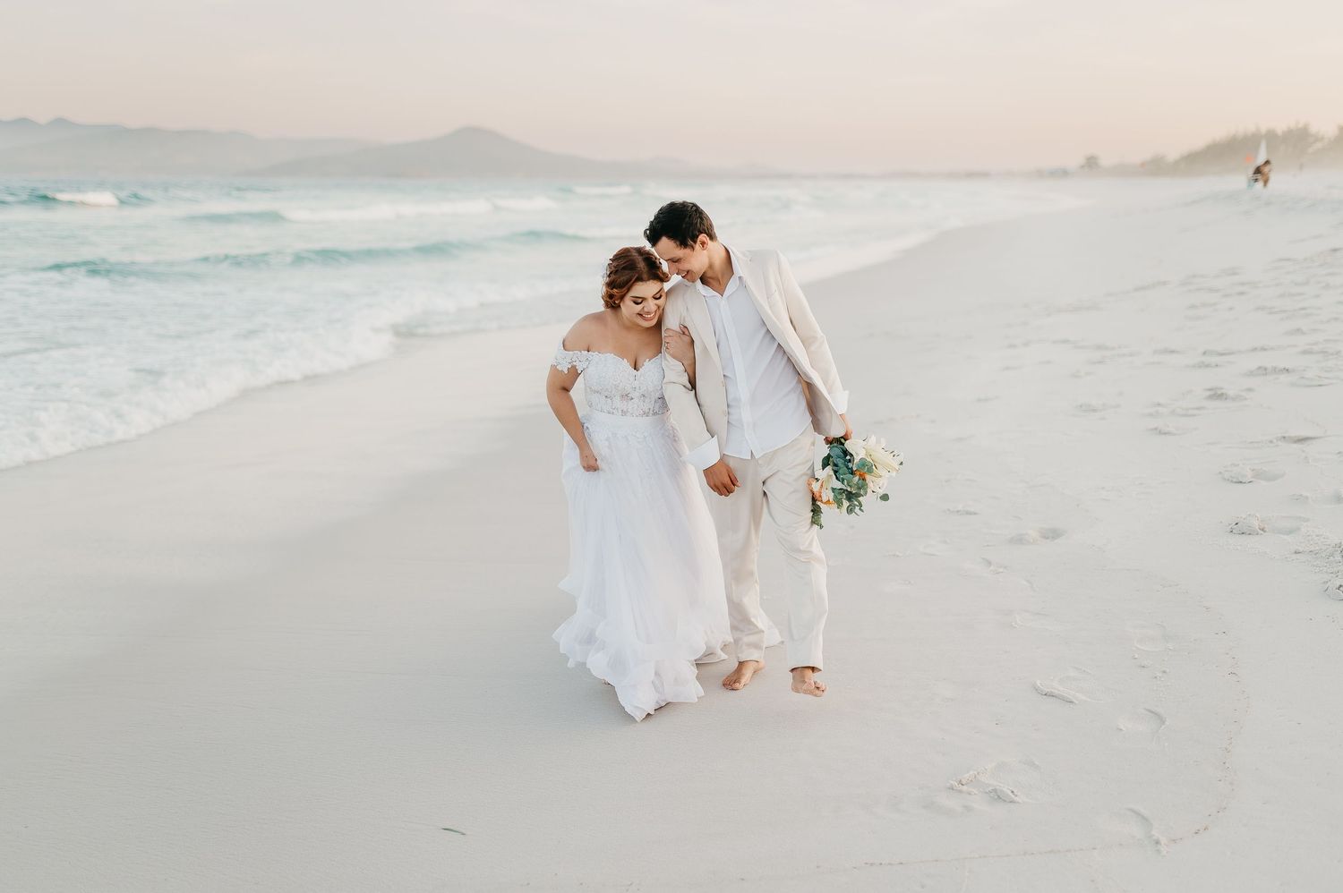 Fotografia de destination wedding em Arraial do Cabo, Rio de Janeiro, noivos caminhando na areia com o mar azul turquesa