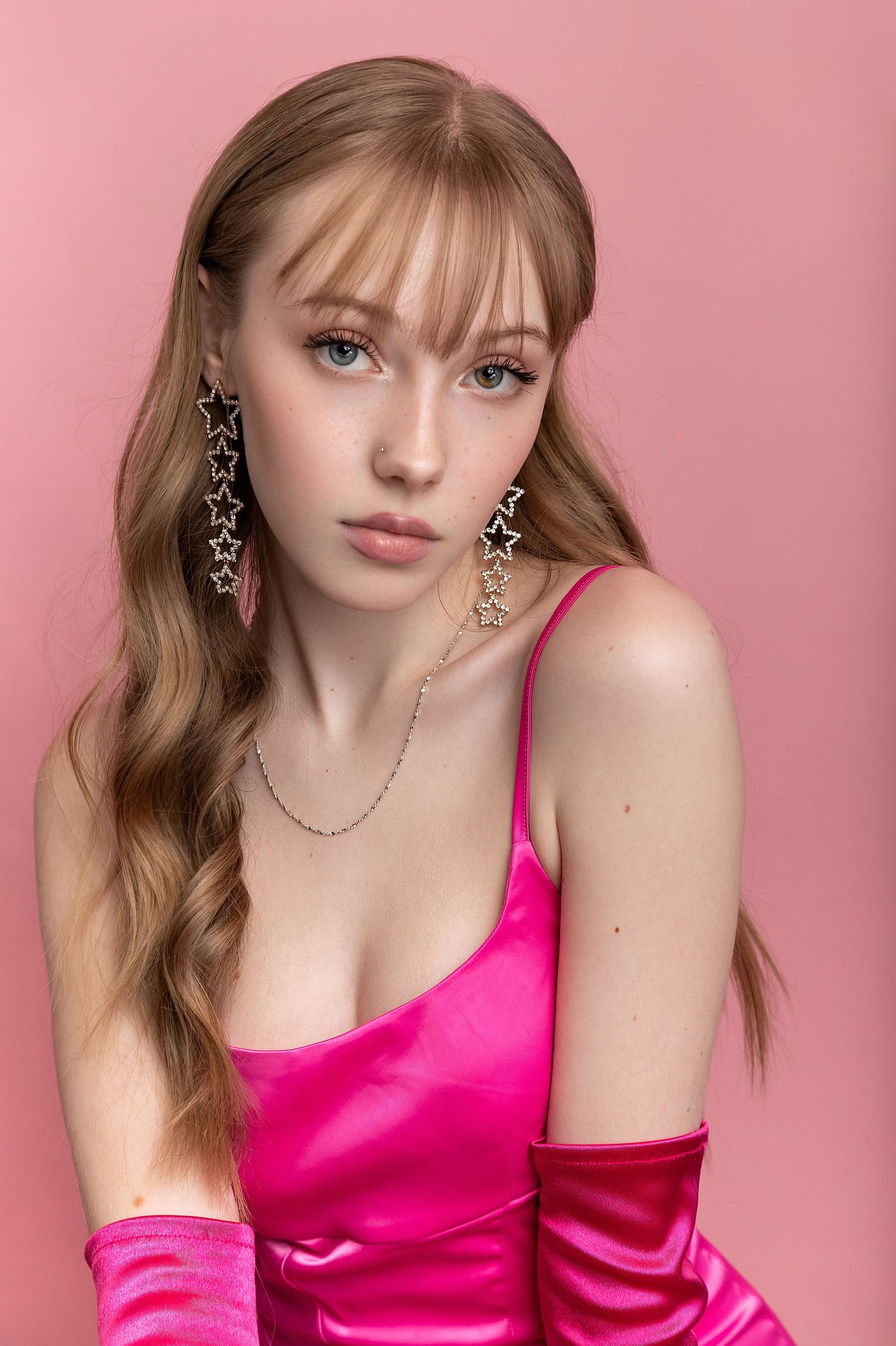 Fashion portrait against pink background featuring bright fuchsia satin dress and delicate star-shaped earrings.