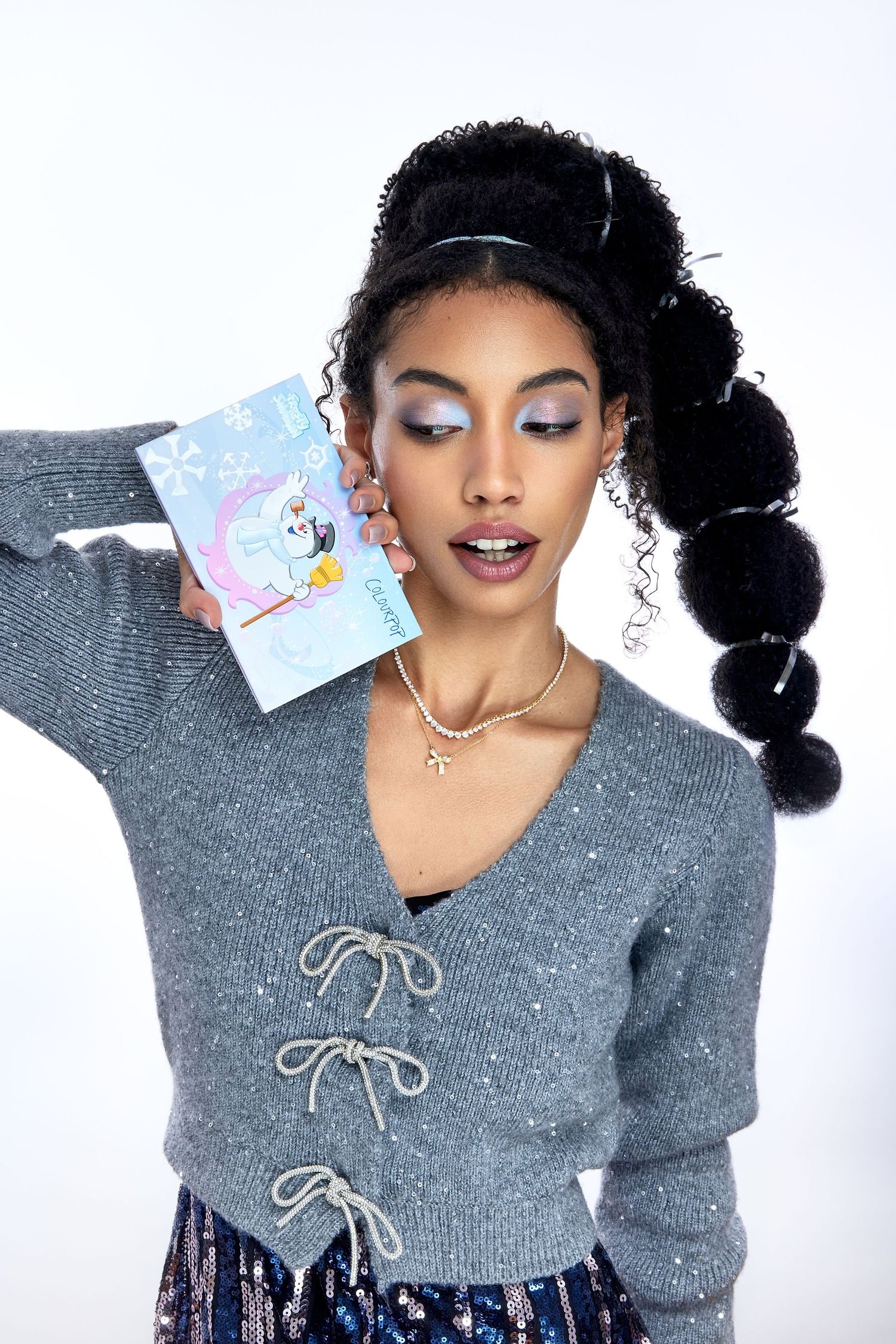 Model wearing a gray lace-up sweater poses against white background in a playful fashion series.