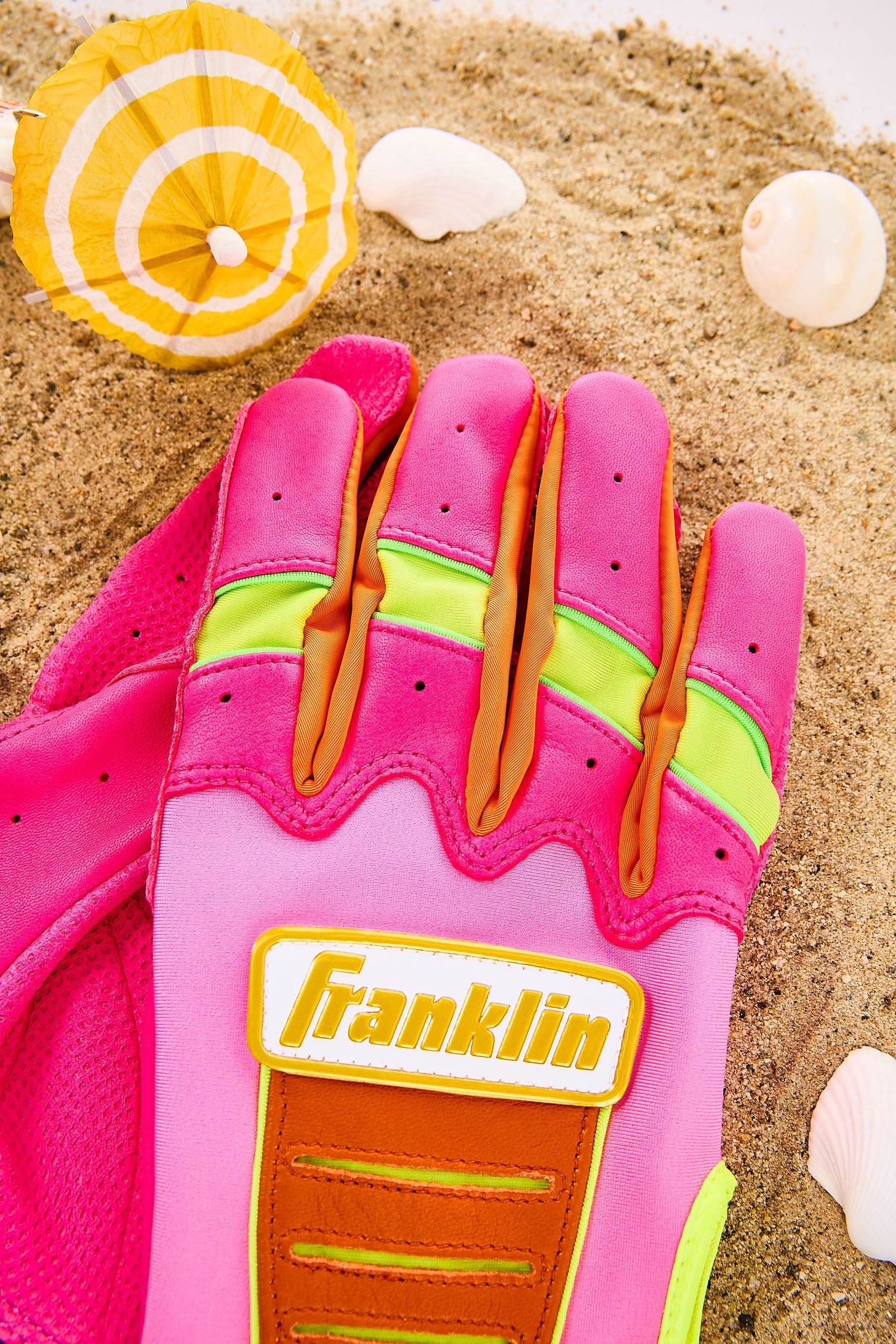 Close-up sequence of a pink and neon yellow Franklin batting glove resting on sandy beach with seashells.