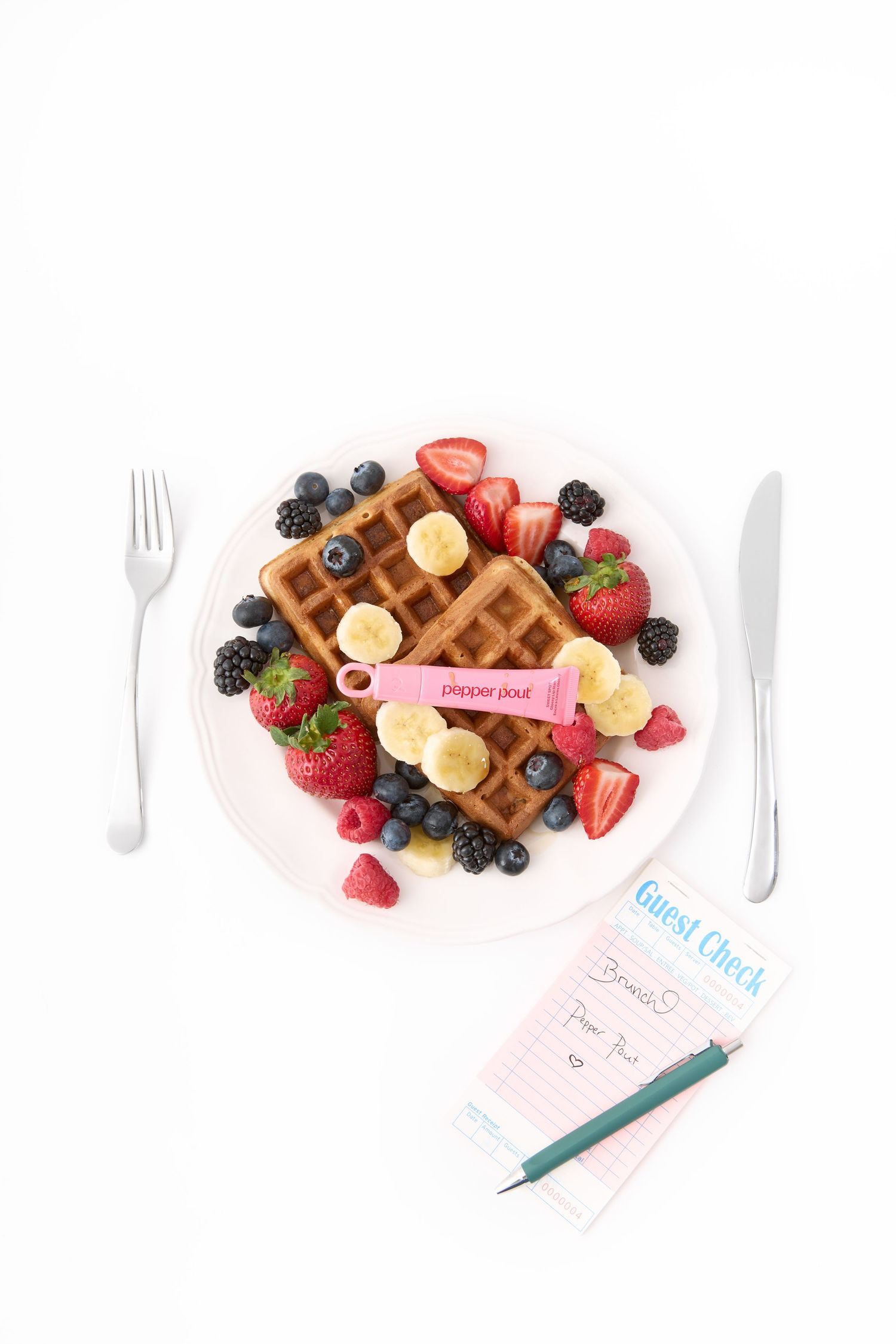 Overhead view of Belgian waffles topped with fresh mixed berries and banana slices on a white plate with a guest check.