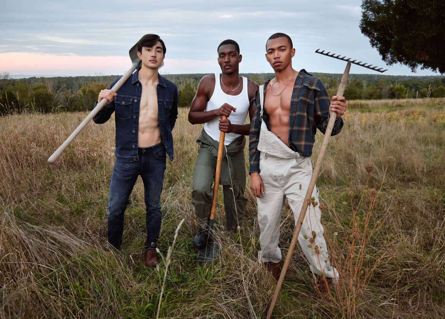 Group of workers with tools and equipment walking through tall grass in rural field.